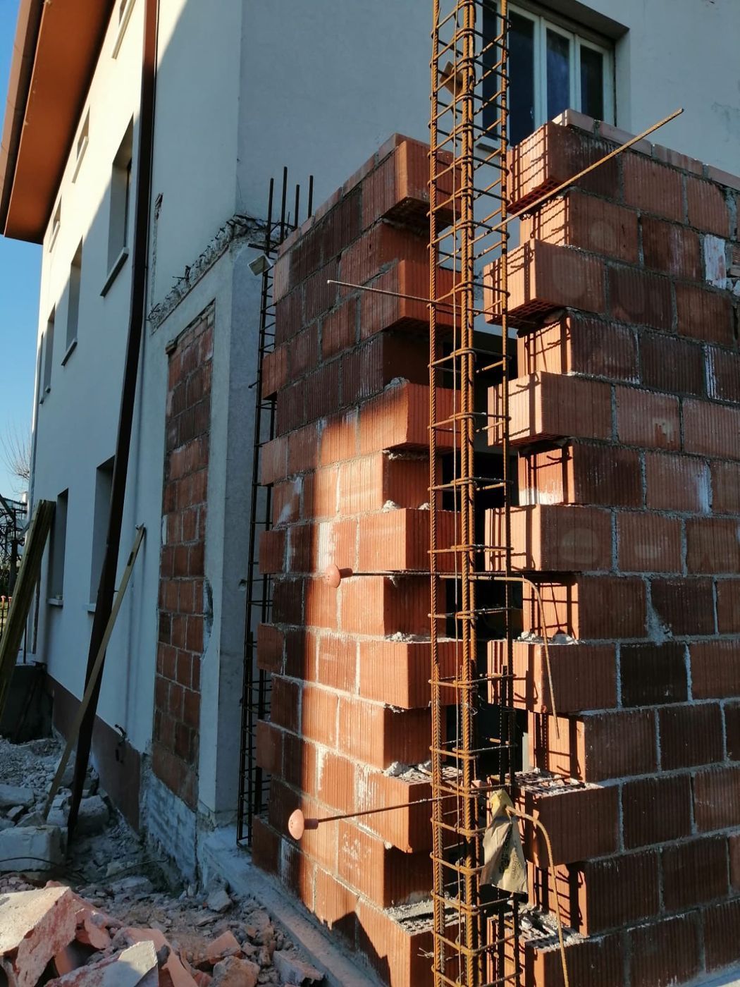 È in costruzione una nuova estensione in mattoni rossi addossata a una casa bianca, con barre d'acciaio verticali a vista.