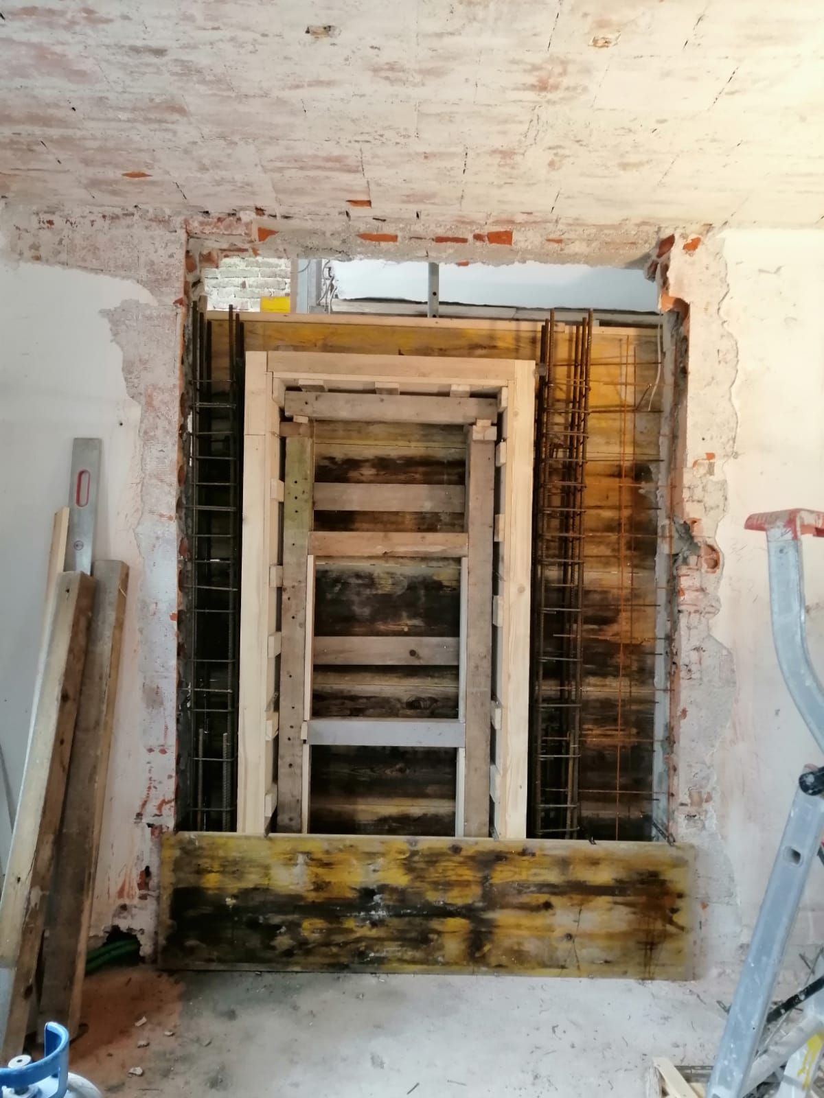 Struttura portante con gabbie di barre d'acciaio e casseforme in legno, inserita all'interno di un'apertura in una parete interna in mattoni.