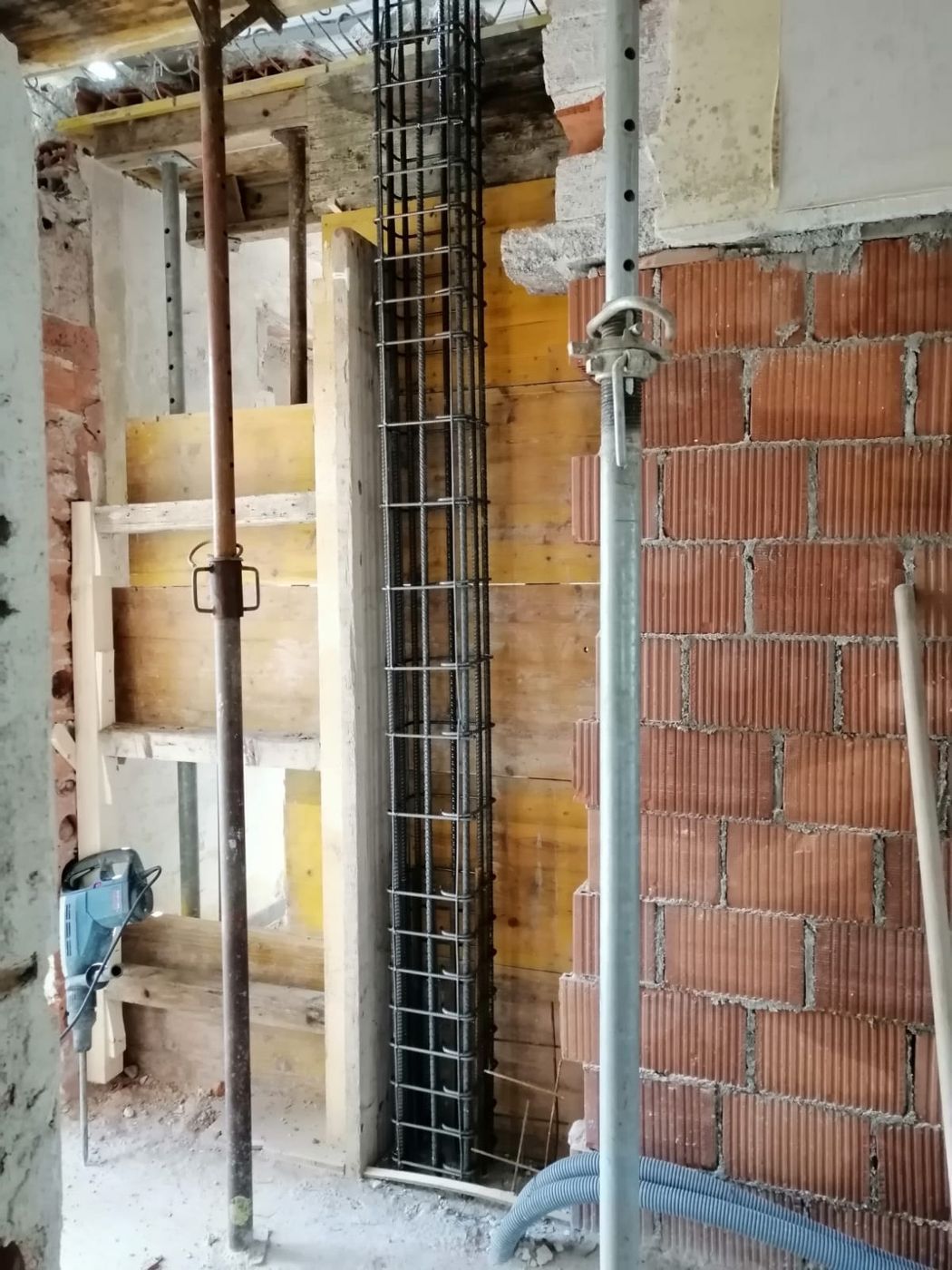 Un cantiere edile che mostra una gabbia di barre d'armatura verticali posizionata tra casseforme in legno e un muro di mattoni.