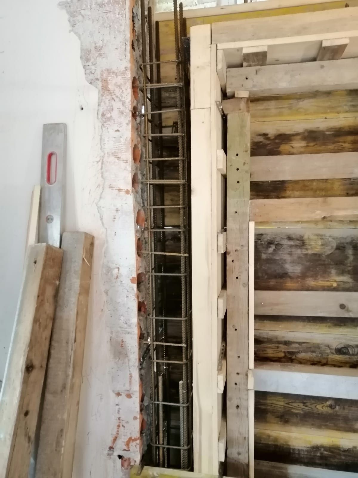 Gabbia verticale in acciaio per barre d'armatura, installata per una colonna in cemento armato accanto a una struttura di casseratura in legno in una stanza in costruzione.