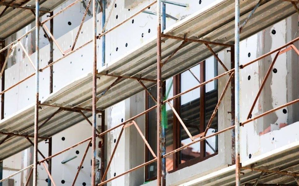 Eine mehrstöckige Metallgerüstkonstruktion umgibt die Außenfassade eines im Bau befindlichen Gebäudes mit Dämmplatten.