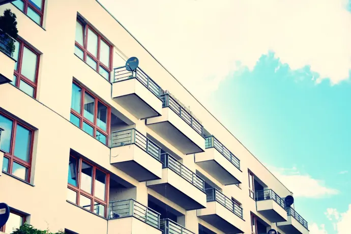 Vista dal basso di un moderno condominio con pareti beige, file di balconi e finestre con cornici scure, sullo sfondo del cielo.