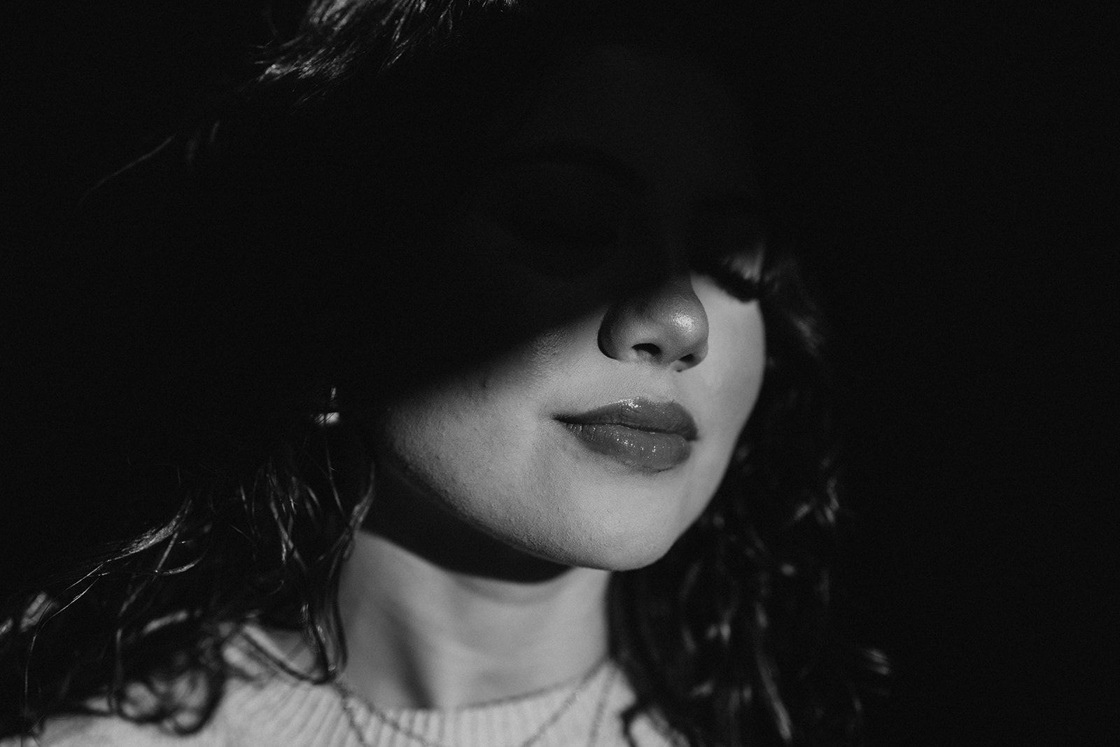 Black-and-white close-up of a person in a dark hat, face partly shadowed, looking downward.