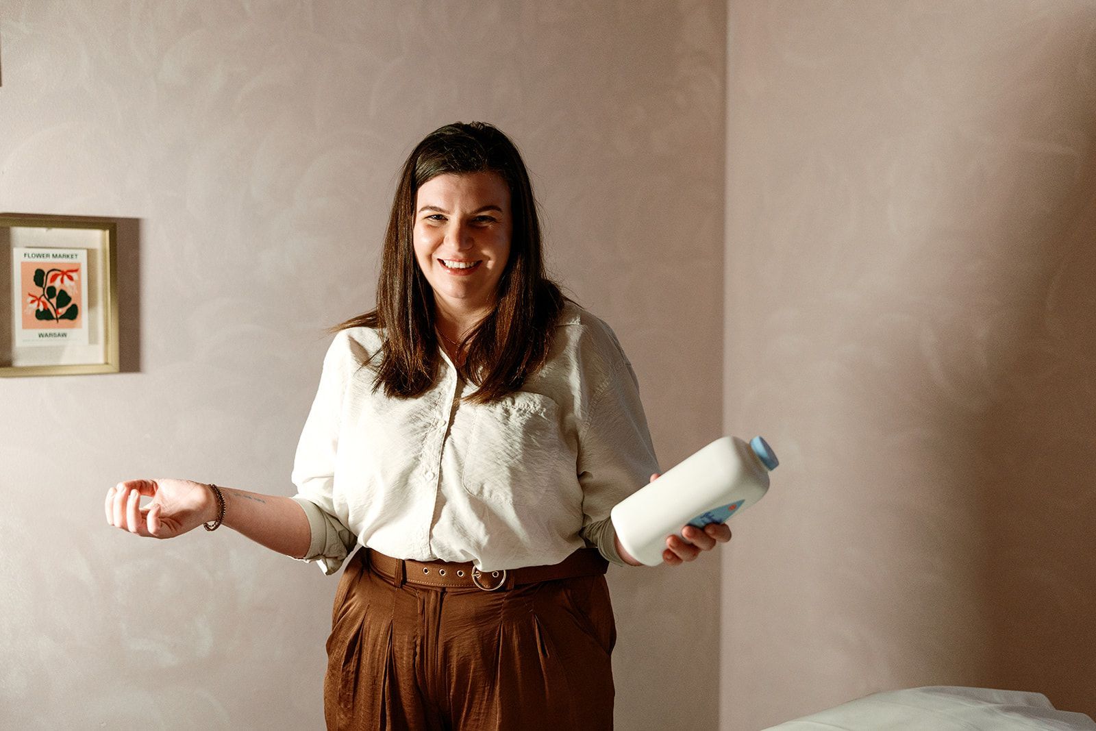 Woman smiling in a room, holding a paint roller and a paint can, with a framed picture on the wall.