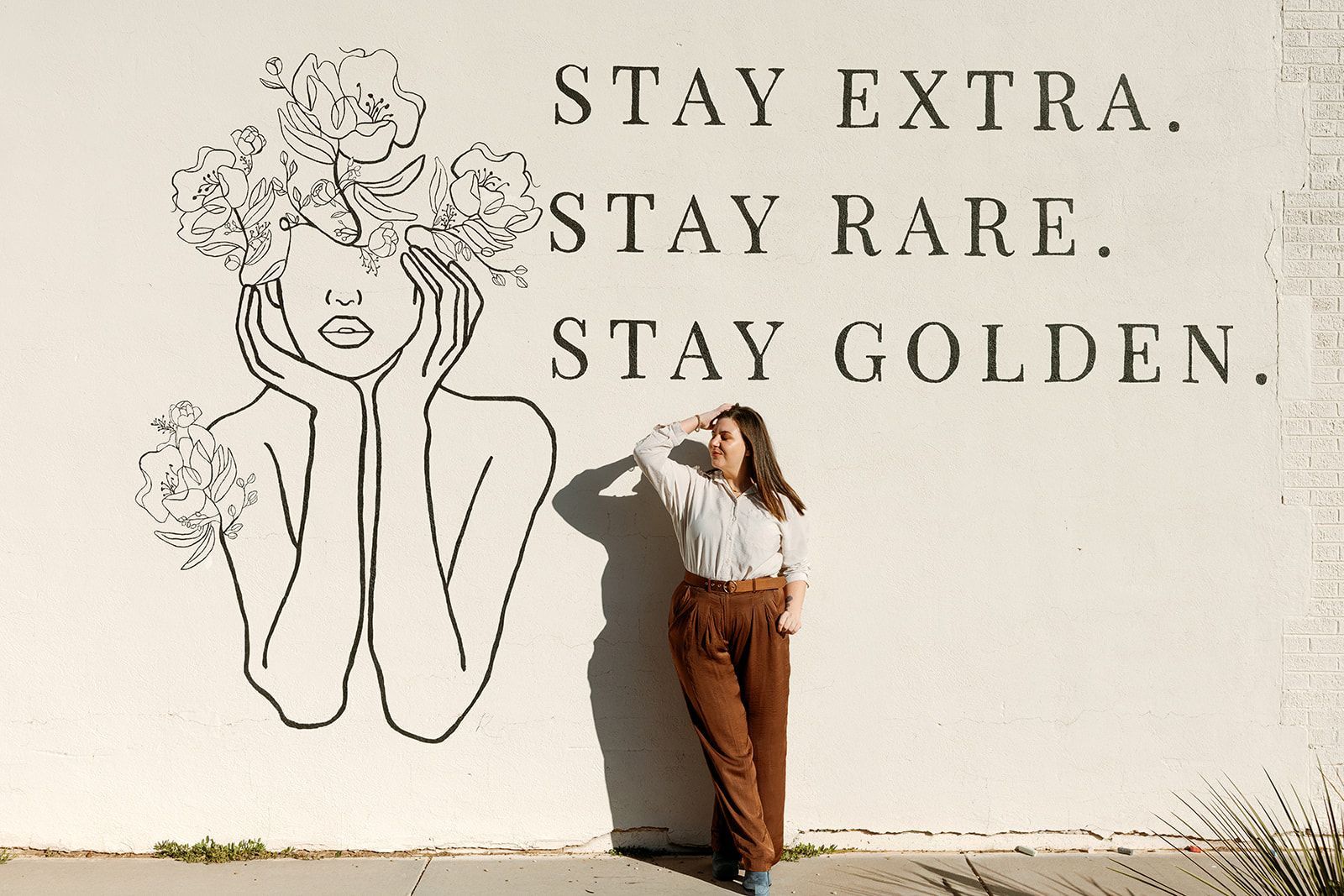Person posing beside mural reading “STAY EXTRA. STAY RARE. STAY GOLDEN.”