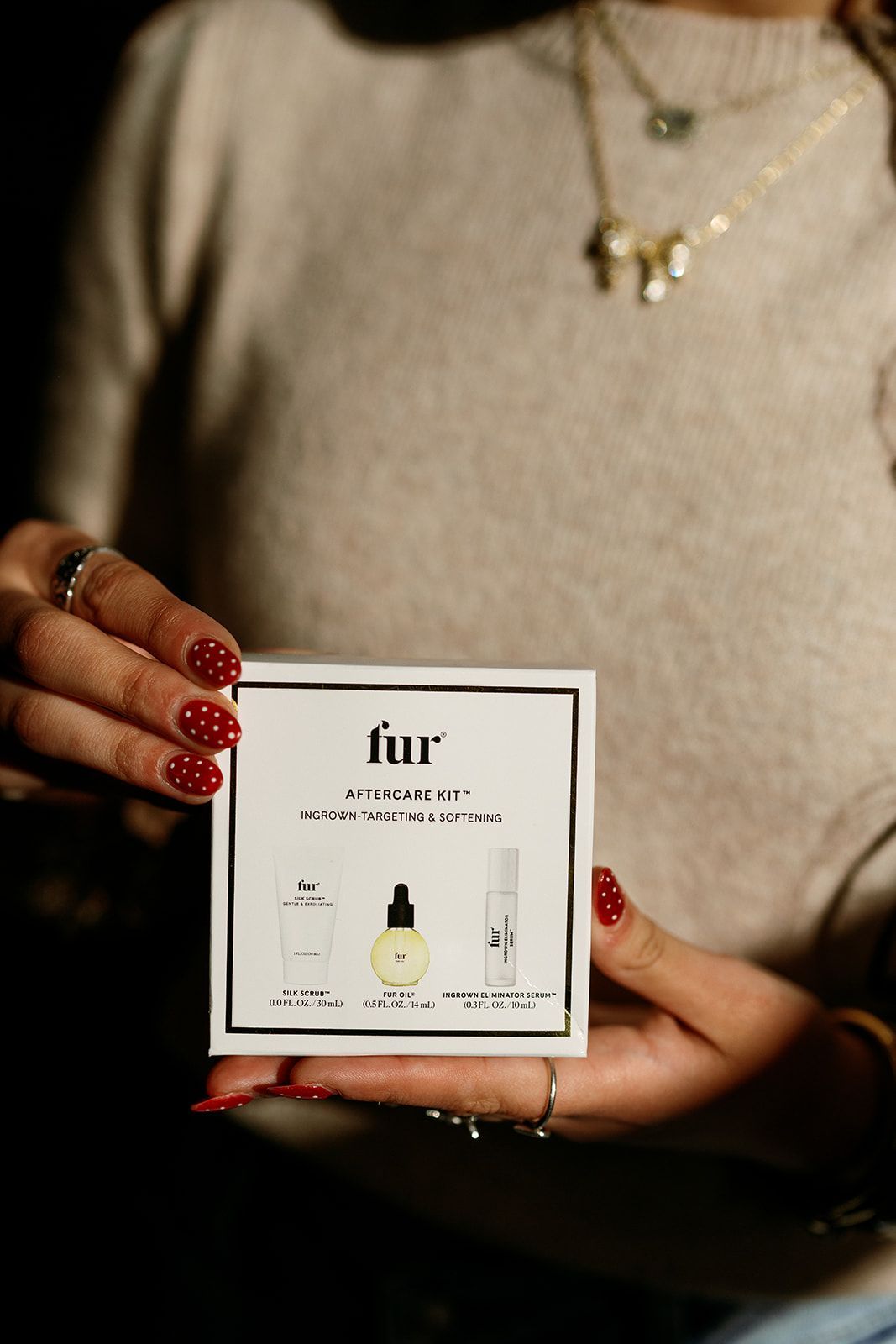 Hands holding a small white Fur skincare box with a dropper bottle, red nails visible.