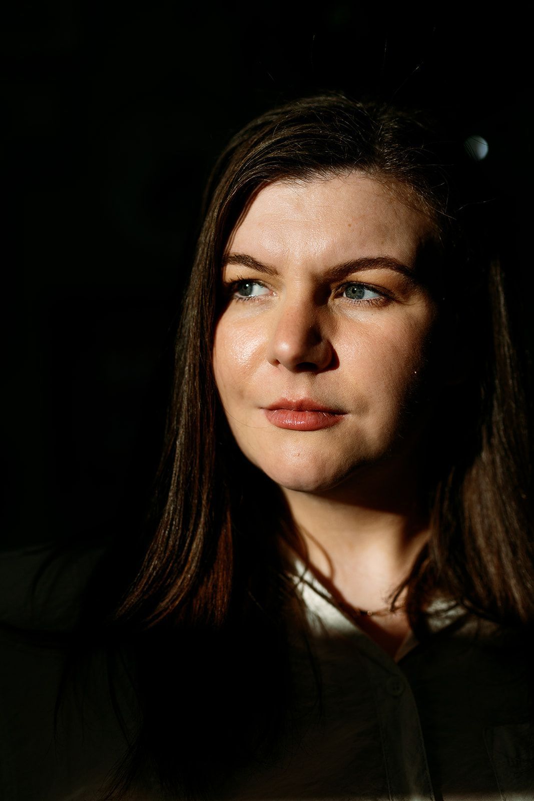 Portrait of a woman with long dark hair, gazing left against a dark background