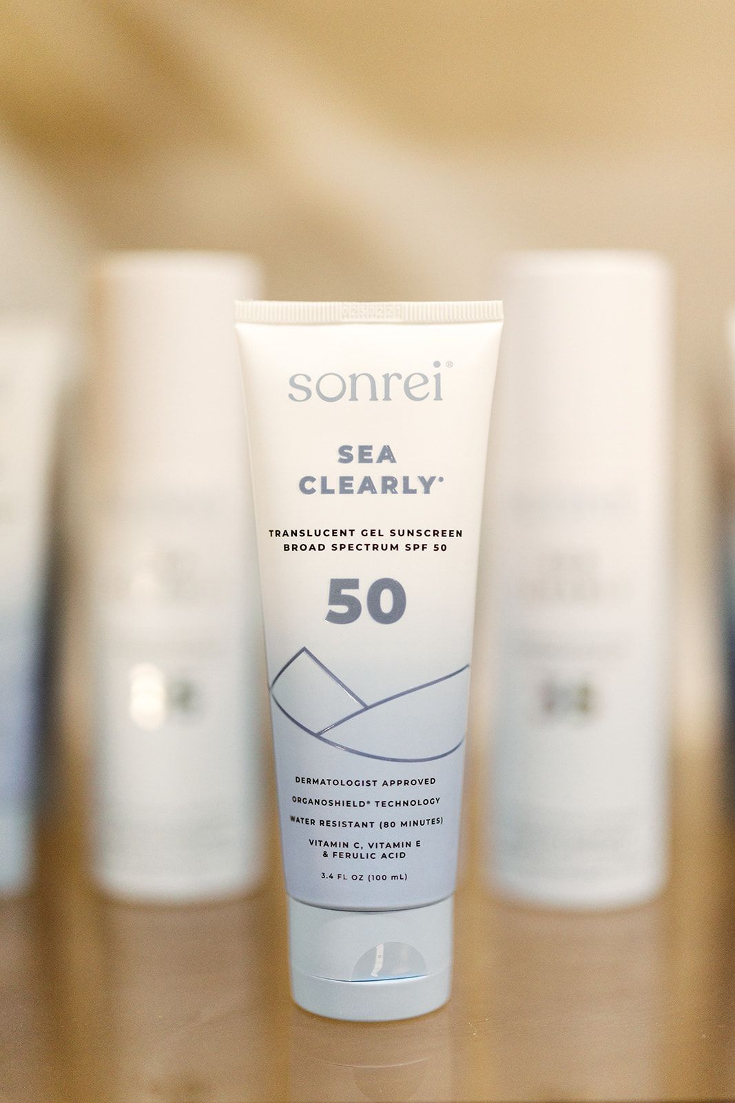 Sunscreen tube labeled “sonrei Sea Clearly 50” on a wooden surface with two blurred bottles behind it