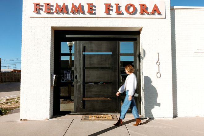 Woman walking into Femme Flora storefront with white facade and dark door