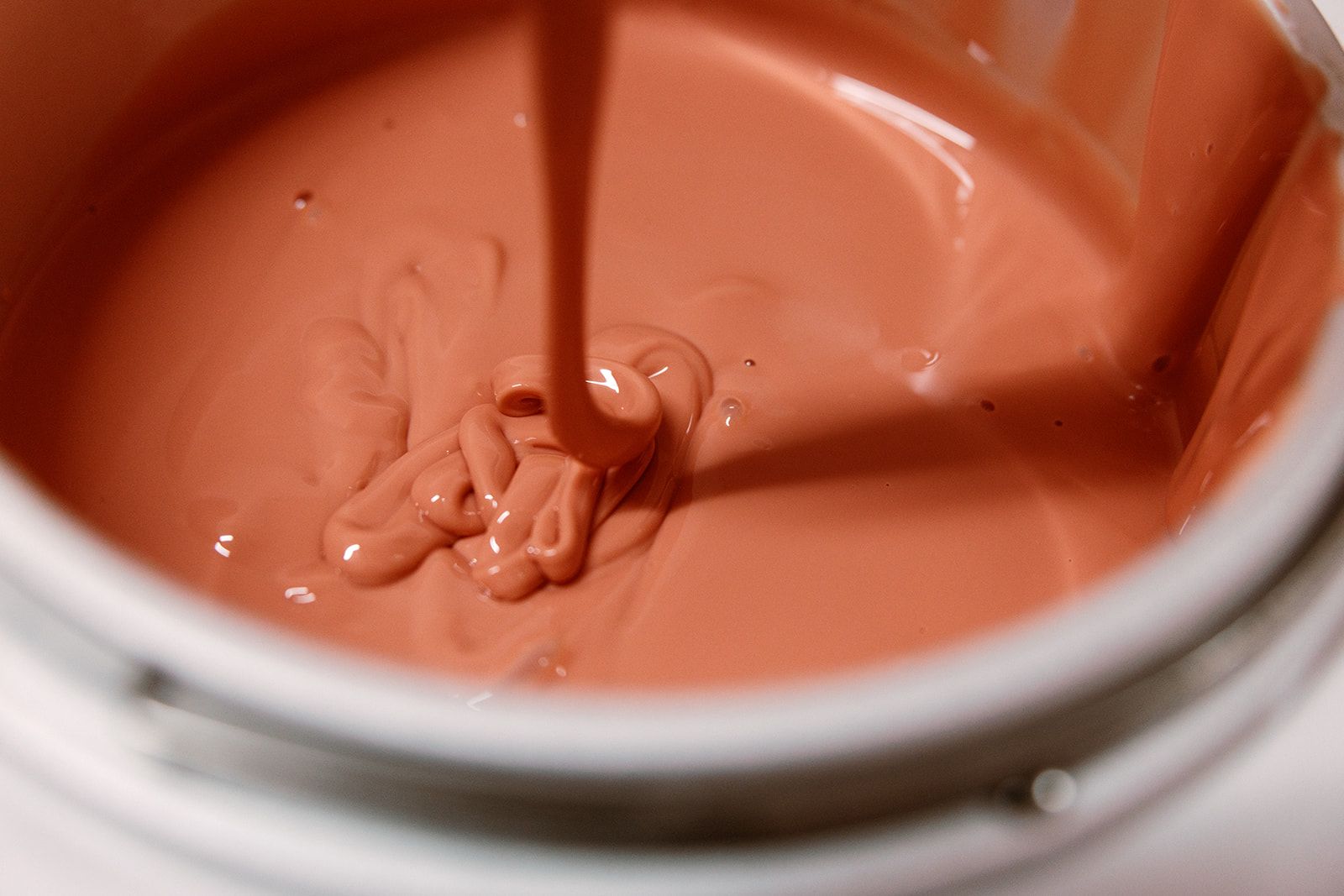 Pink paint being poured into a can, creating a swirl on the surface.