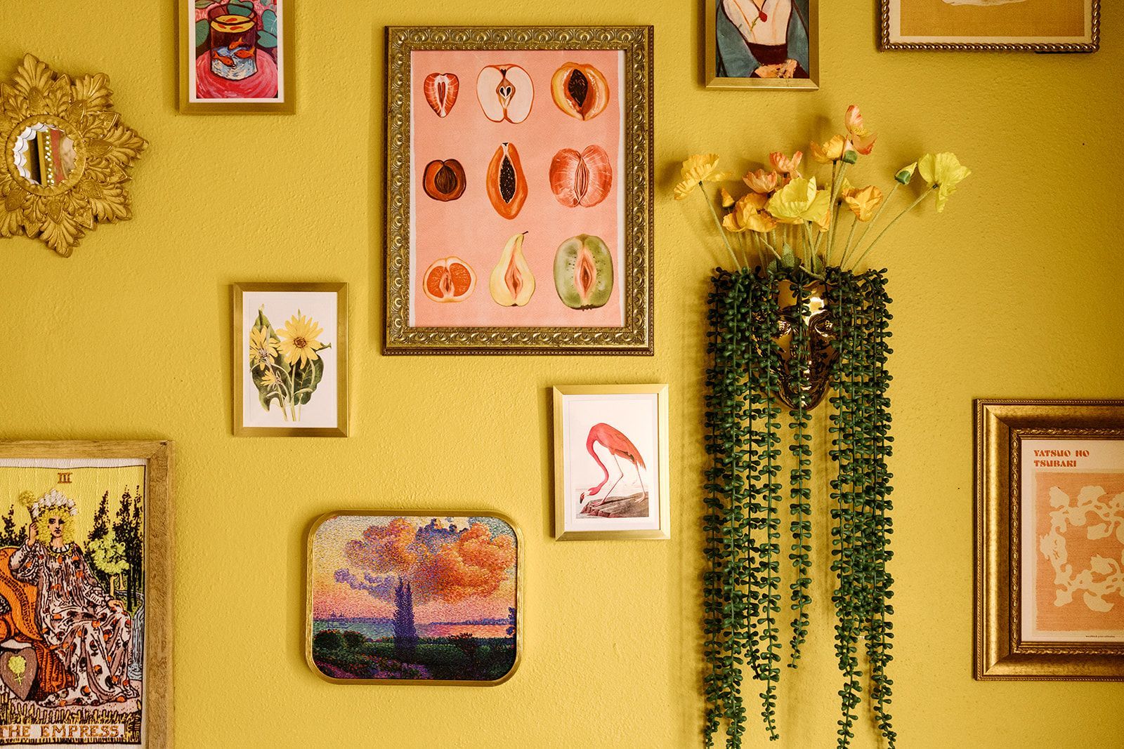 Yellow wall with framed art, a small landscape print, and hanging trailing plant decor