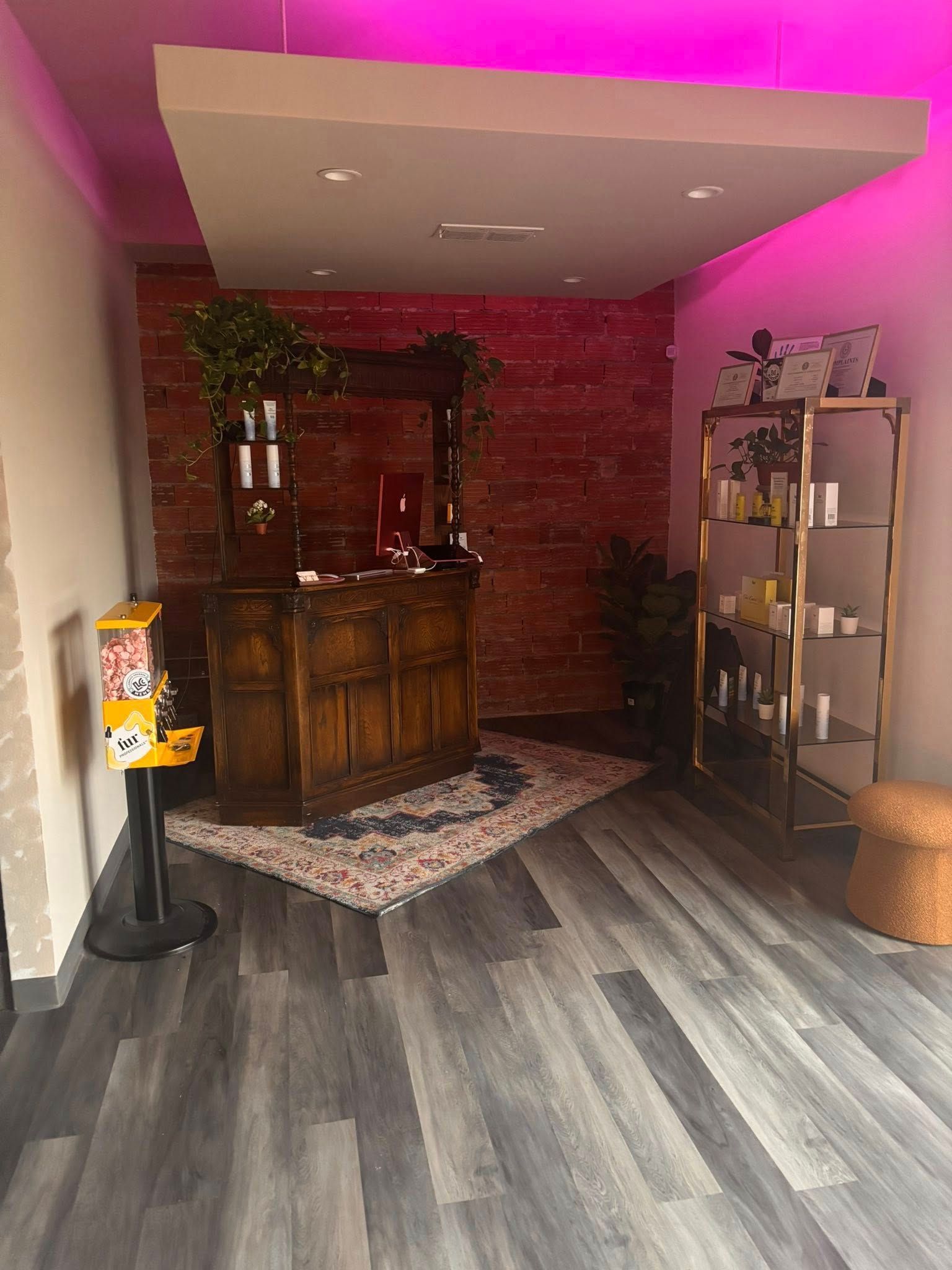 Reception area with wooden counter, brick wall, and shelving. Gray wood-look floor, purple lighting.