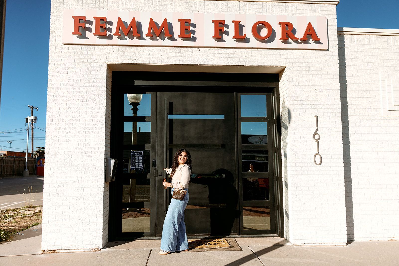 Person standing in a doorway beneath the Femme Flora sign on a sunny street