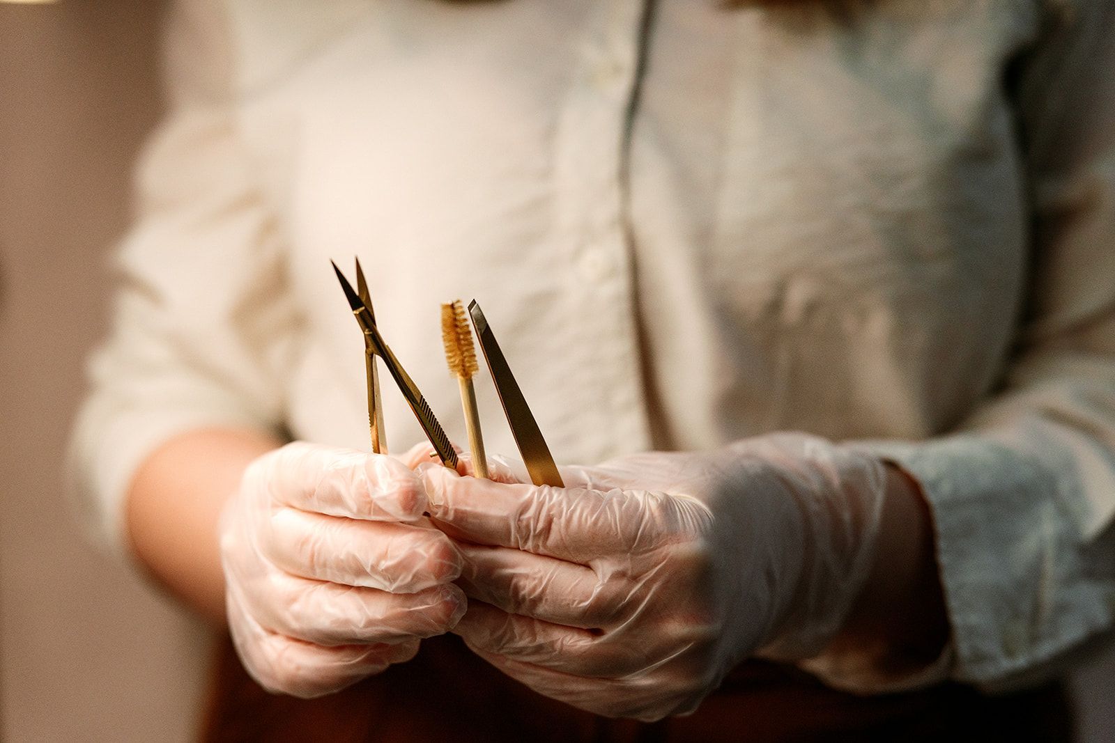 Gloved hands holding three thin tools or tweezers over a blurred work surface