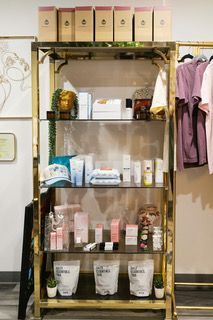 Shelved display of boxed and bottled products in a salon or spa, with towels and robes hanging nearby
