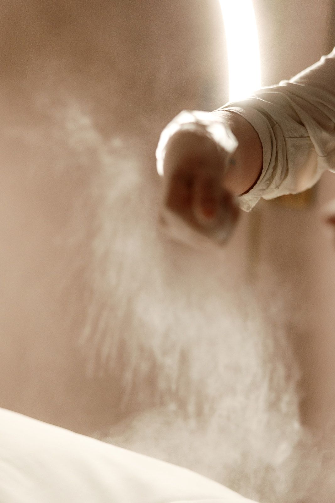 A hand in a white sleeve brushing a beige wall with dust or powder swirling.
