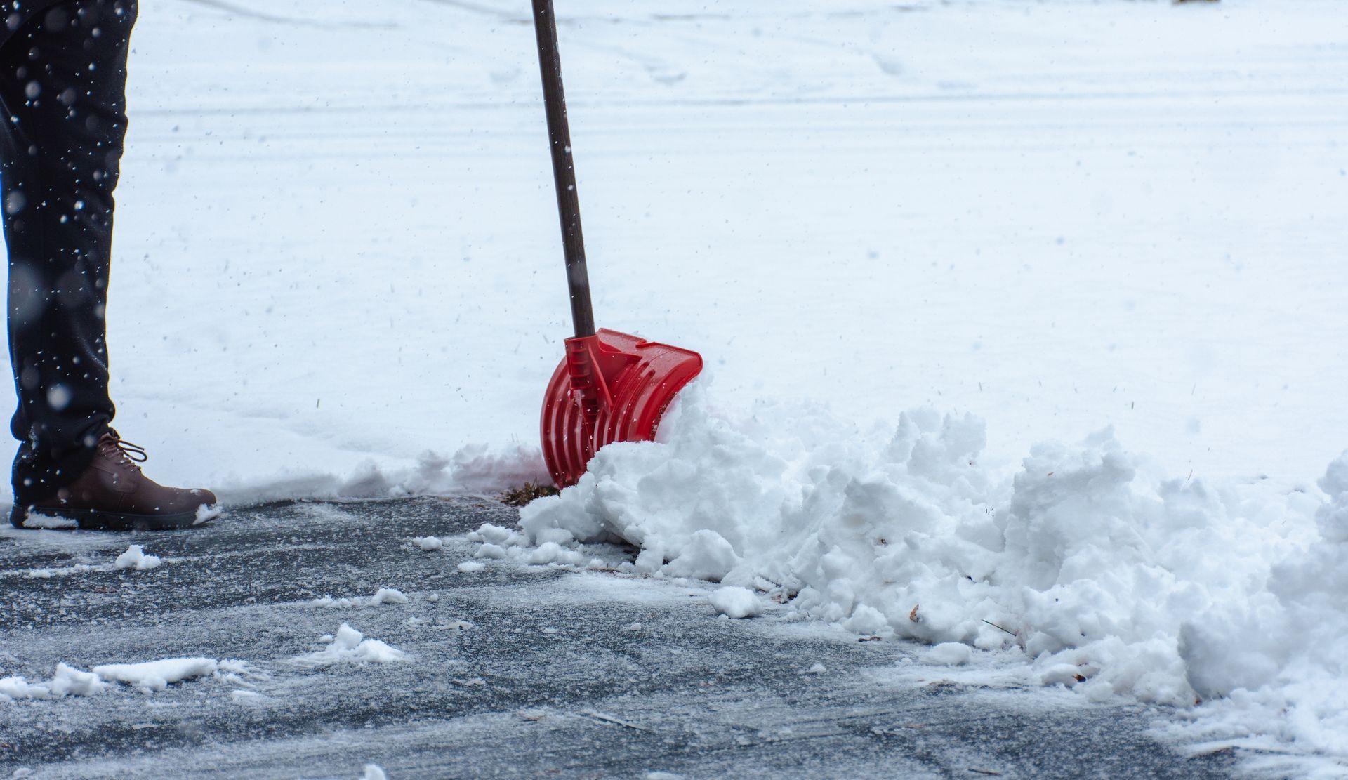 Person shovels snow with a red shovel on a snowy driveway. Person shovels snow with a red shovel on a snowy driveway.