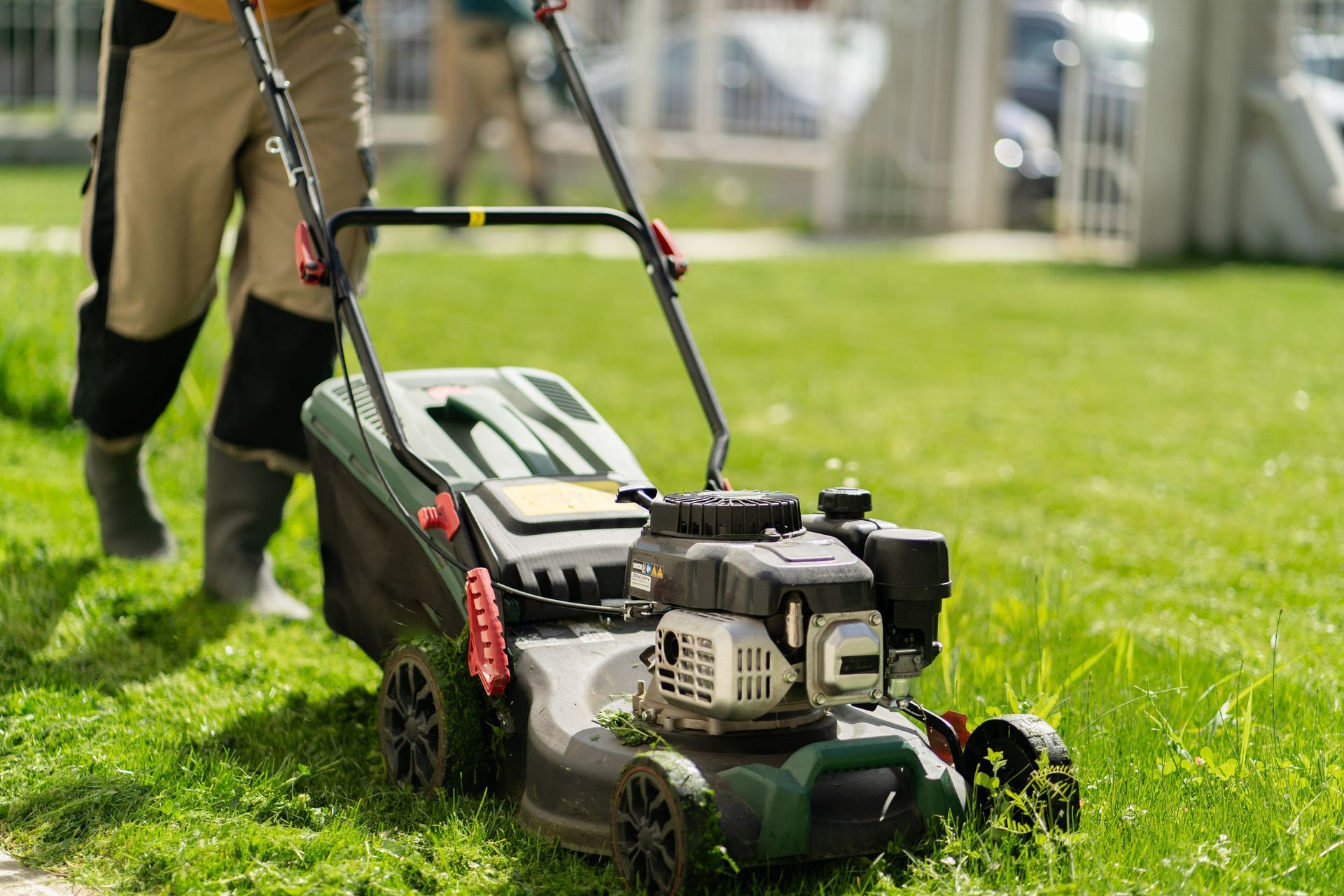 Person mowing a green lawn with a gas-powered lawnmower on a sunny day. Person mowing a green lawn with a gas-powered lawnmower on a sunny day.