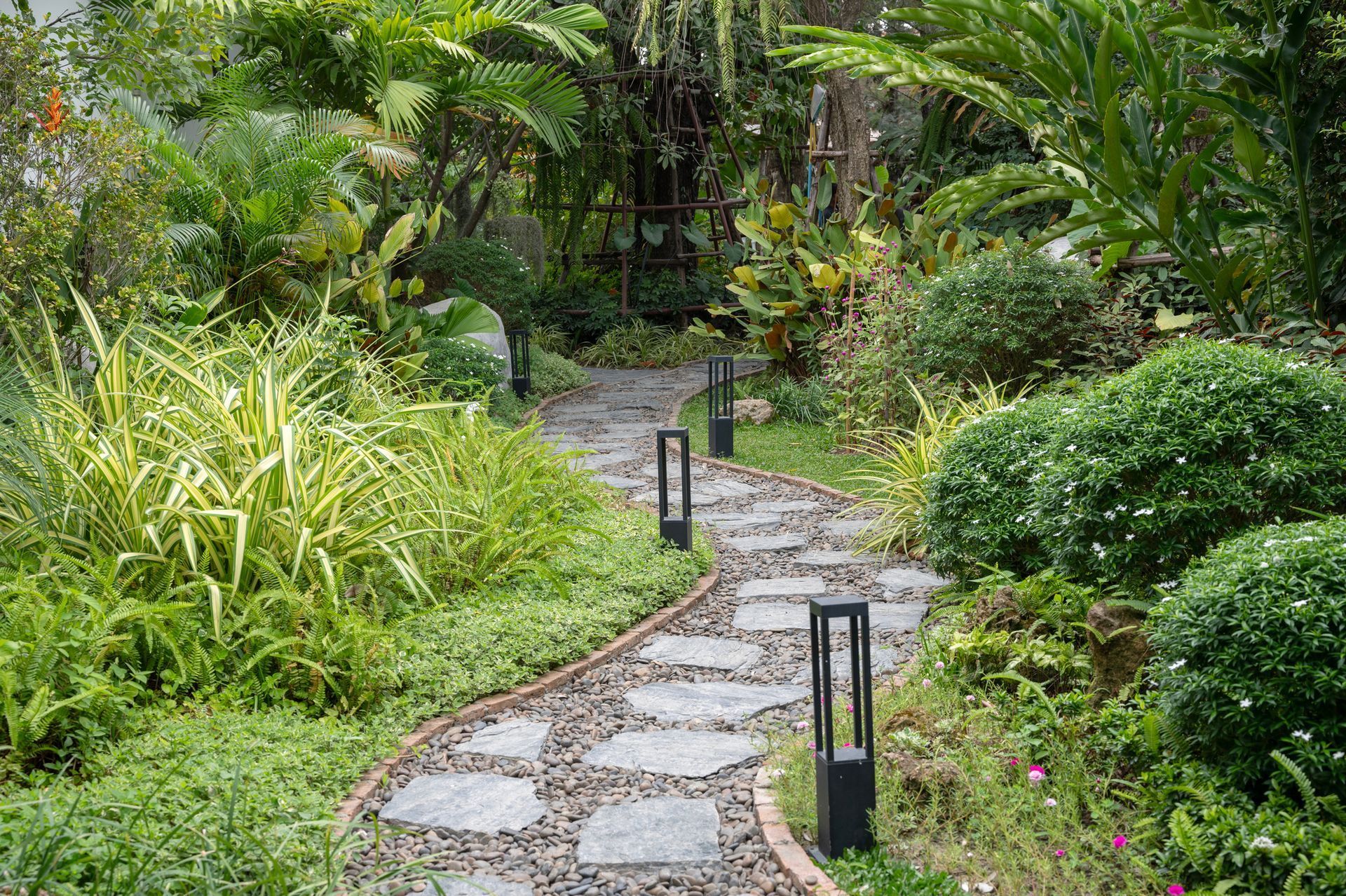 Stone path winds through lush, green garden with low lighting fixtures. Stone path winds through lush, green garden with low lighting fixtures.
