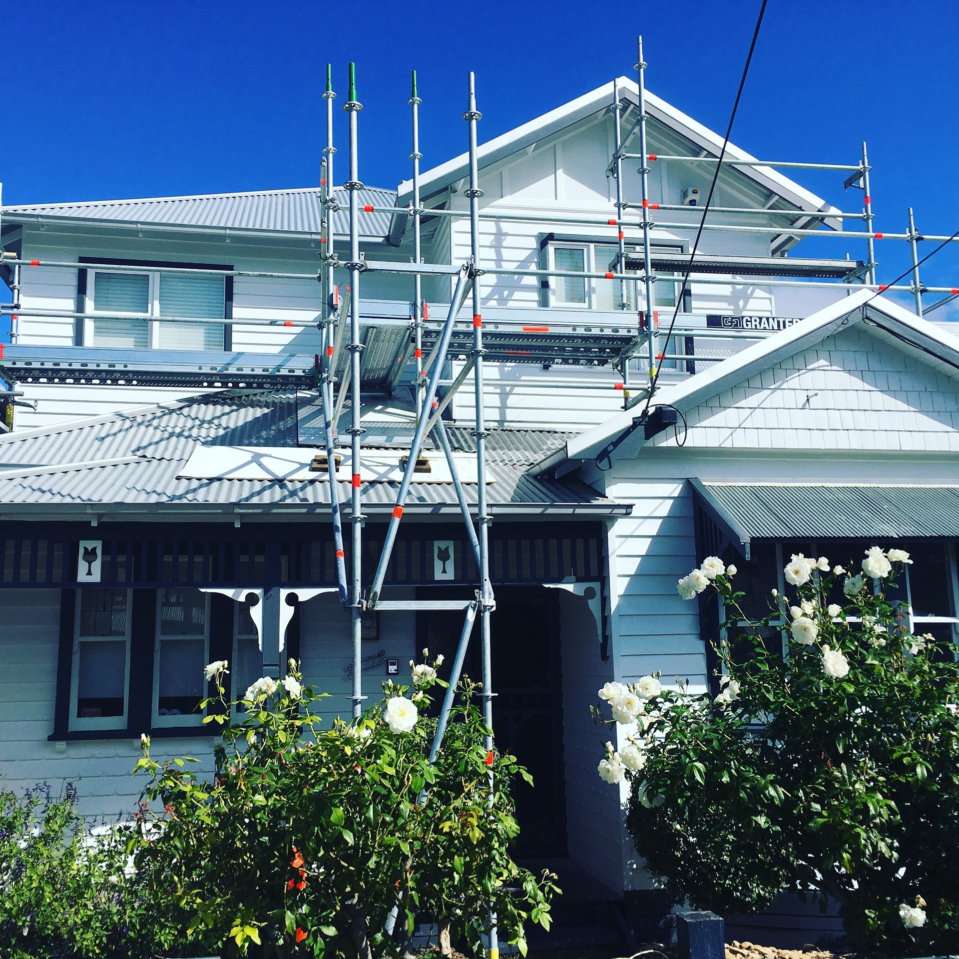 House undergoing renovation with scaffolding. White exterior, blue sky, roses in the foreground.