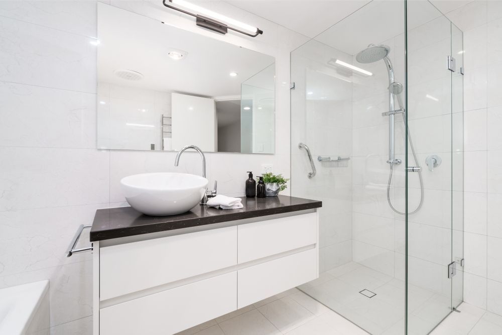 A bathroom with a sink , mirror and walk in shower.