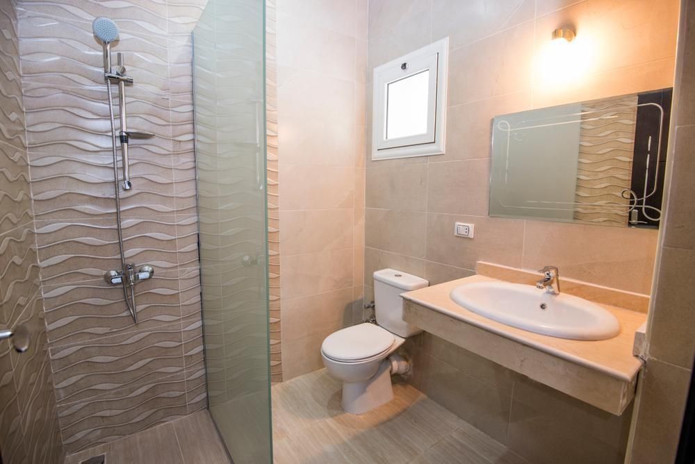 A bathroom with a toilet , sink , shower and mirror.