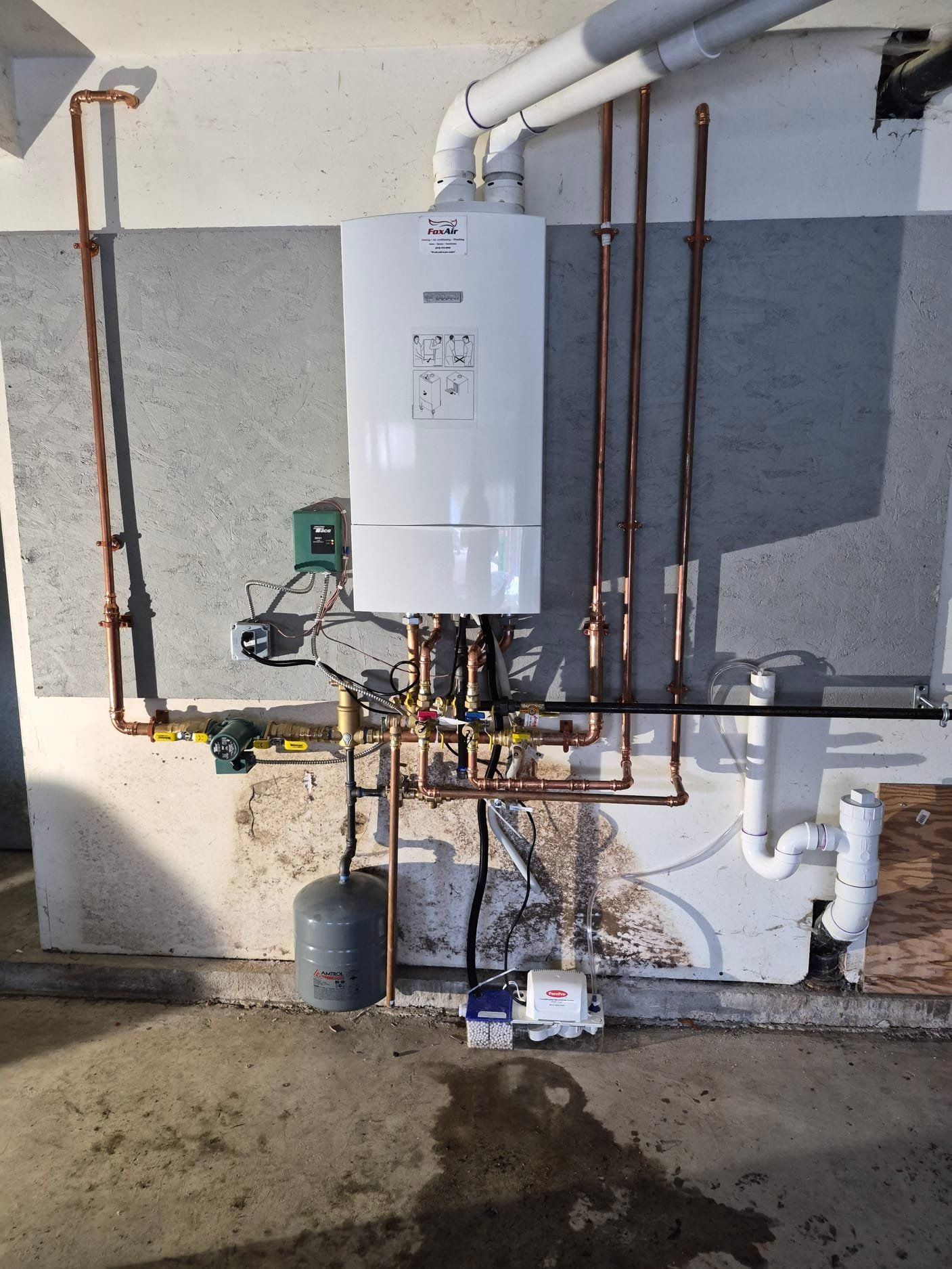 Wall-mounted water heater with pipes and valves in a utility area against a gray concrete wall.