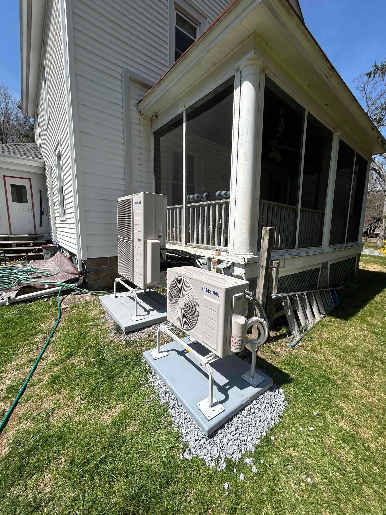 Outdoor home side yard with two HVAC units on concrete pads beside a screened porch and white siding.