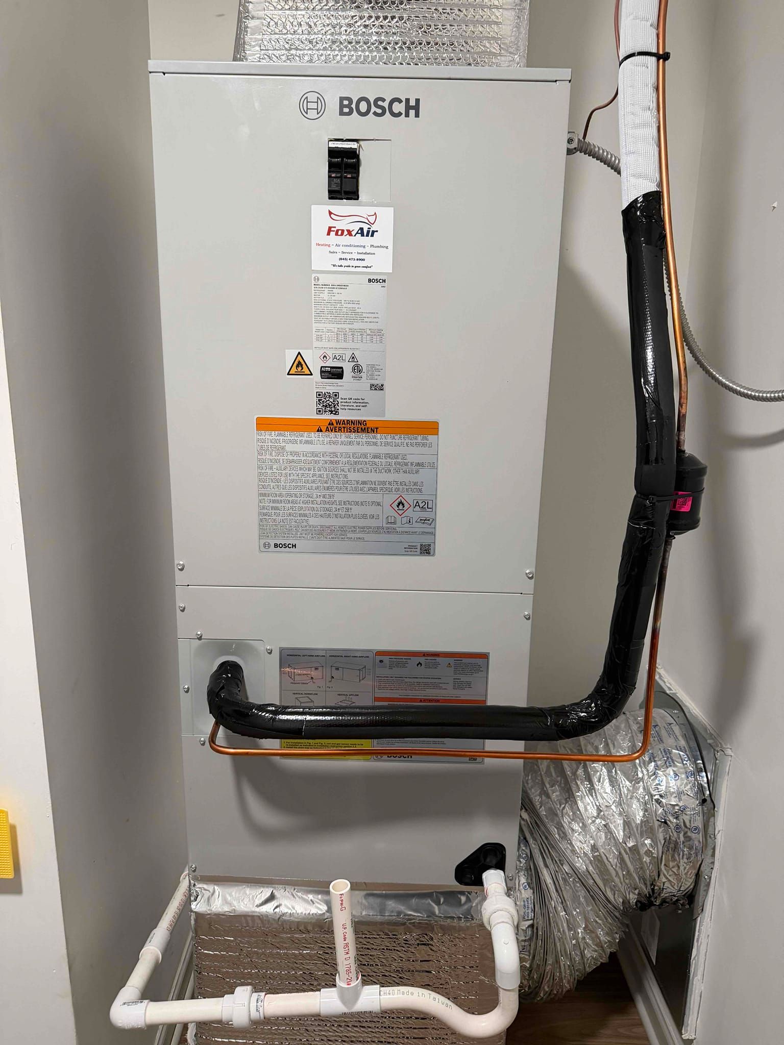 Bosch wall-mounted water heater with black piping in a utility room, above a white laundry sink.