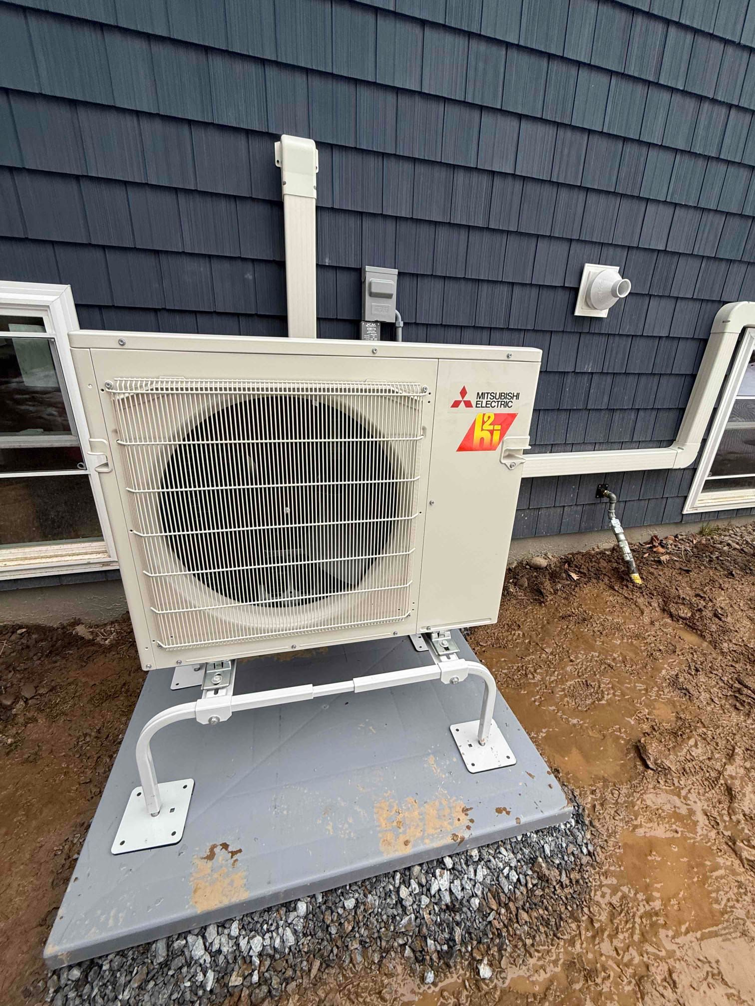 Outdoor heat pump unit mounted on a concrete pad beside a dark siding house