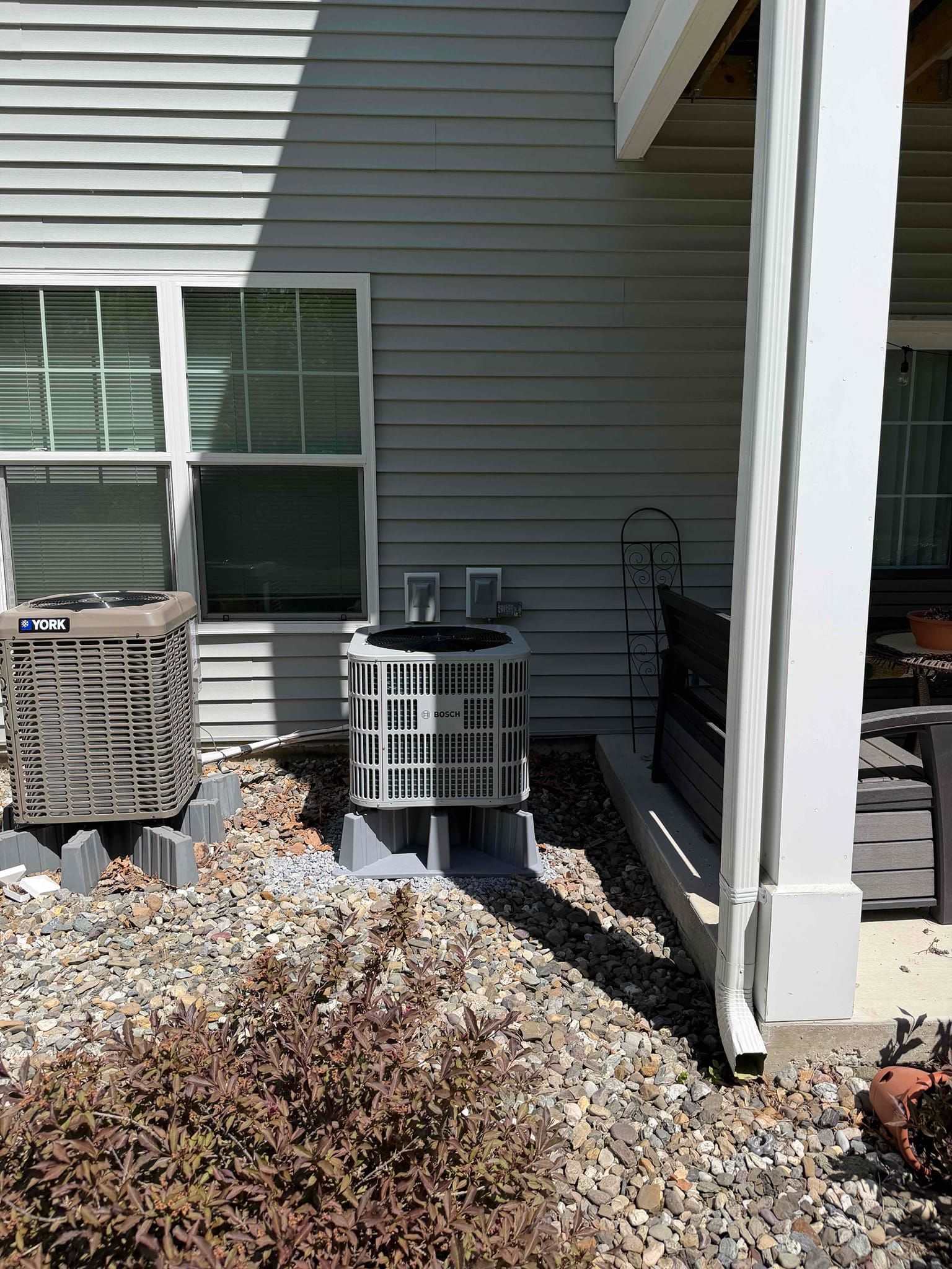 Back patio with white siding, window, air conditioners, and a gravel bed with shrubs
