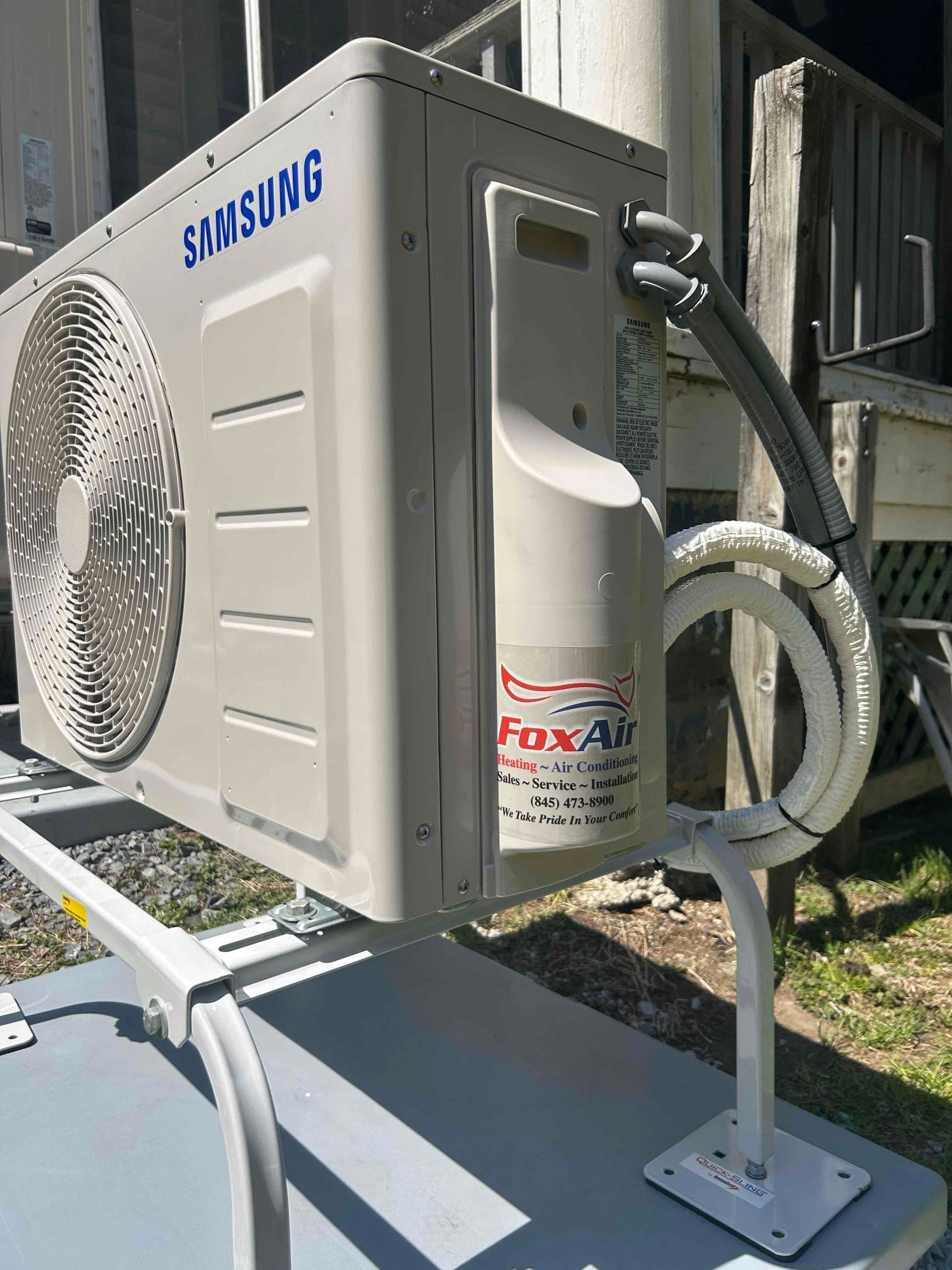 Samsung outdoor air conditioner unit mounted on a metal stand beside a house wall