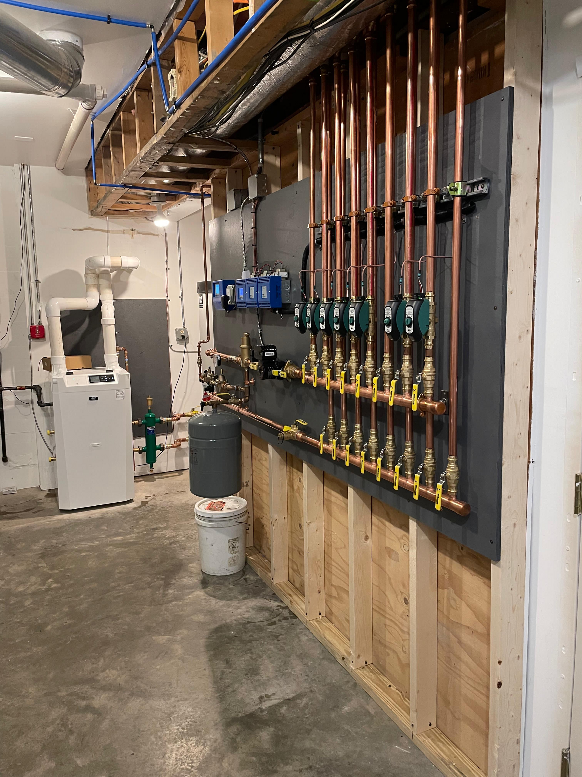 Mechanical room with exposed copper pipes, wall-mounted pumps, and utility equipment along a concrete floor