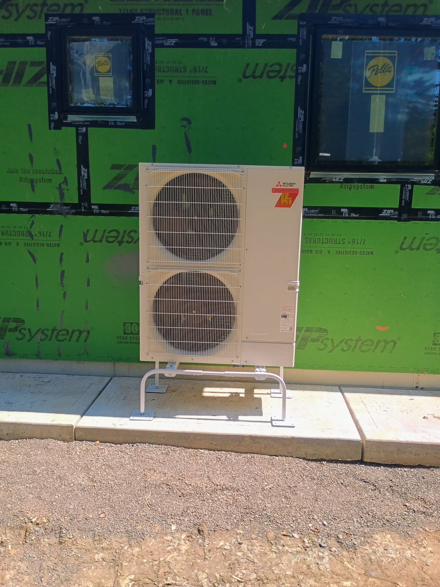 Outdoor HVAC unit with two fans beside a green construction wall in bright sunlight
