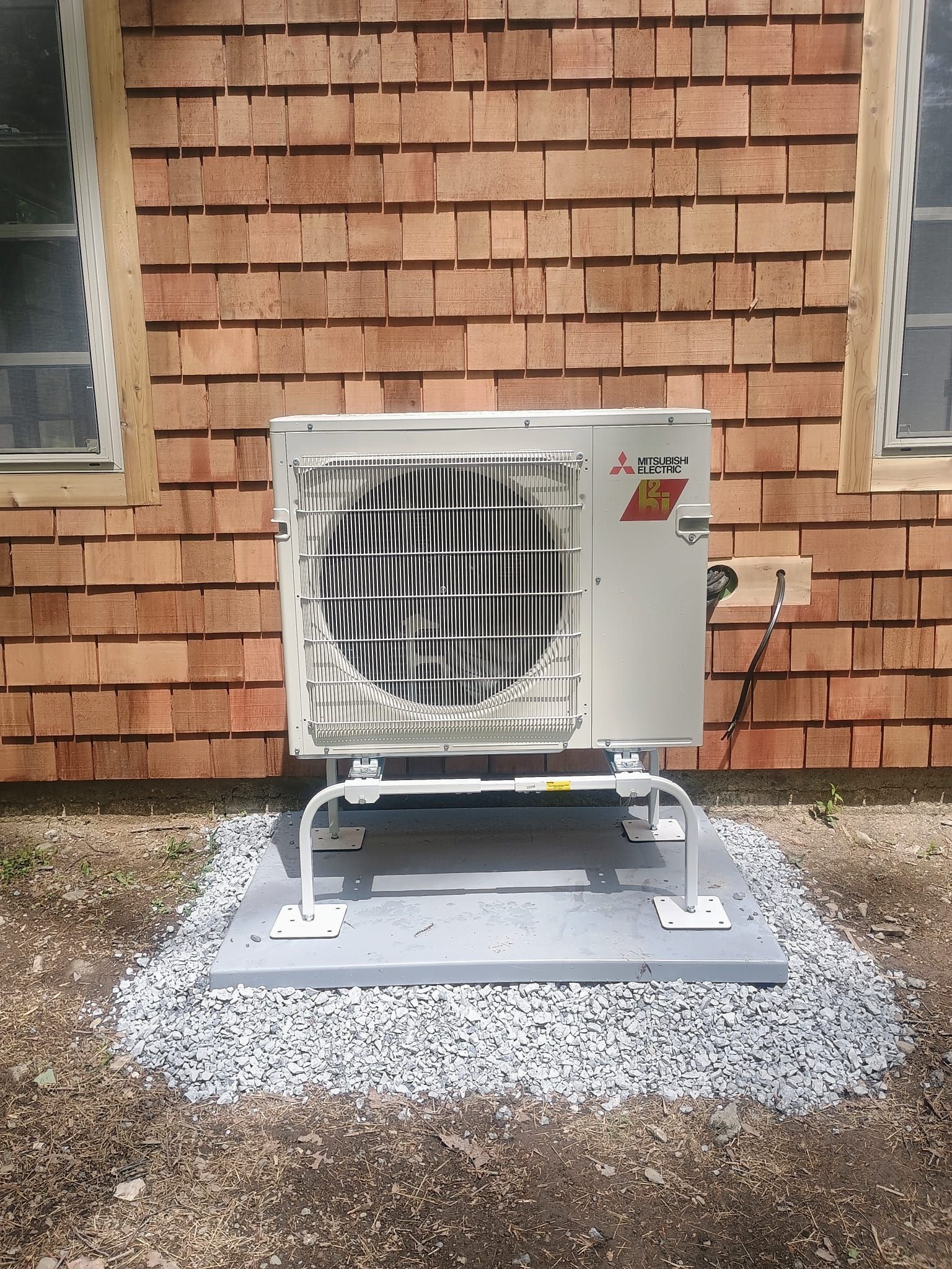 Outdoor air conditioner unit on a stand against a brick wall, set on gravel.