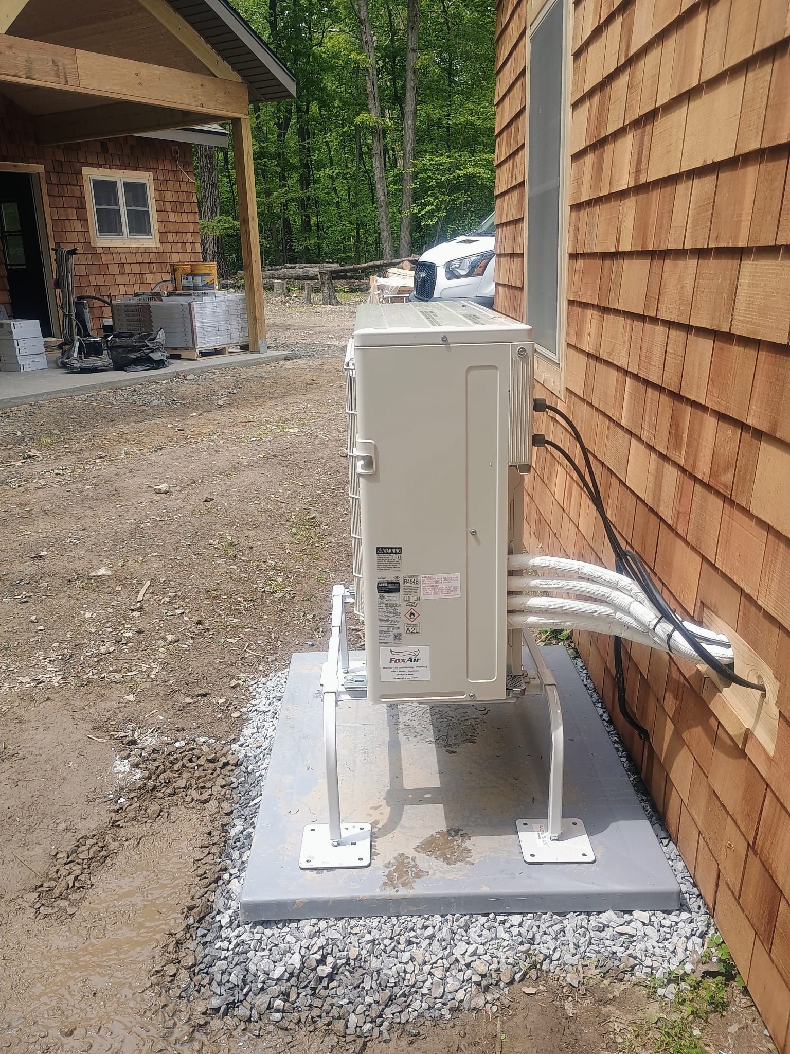 Outdoor utility box on a concrete pad beside a house, with white conduit pipes and gravel ground.
