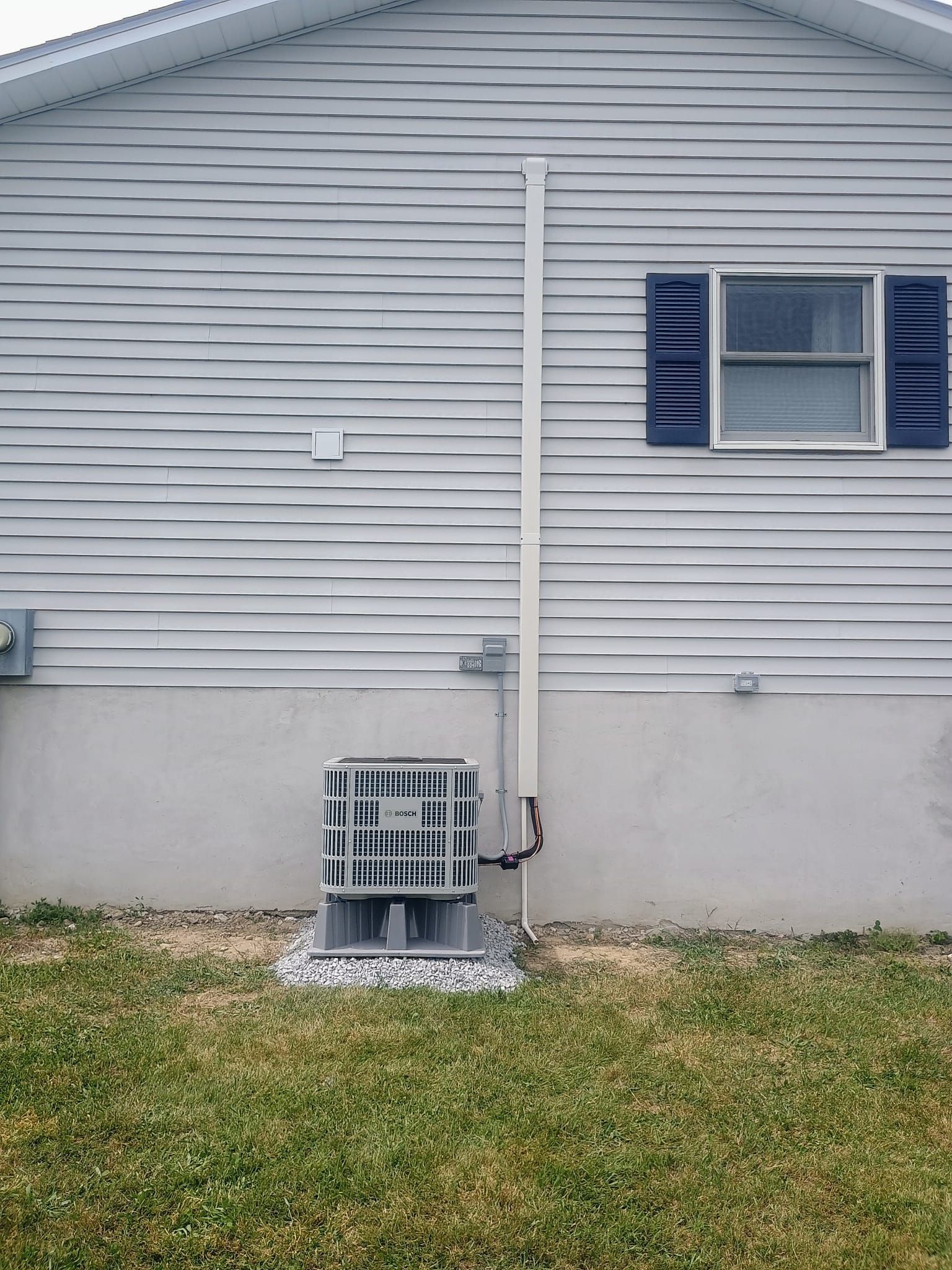 House exterior with gray siding, blue shutters, and an air conditioner unit near the foundation.