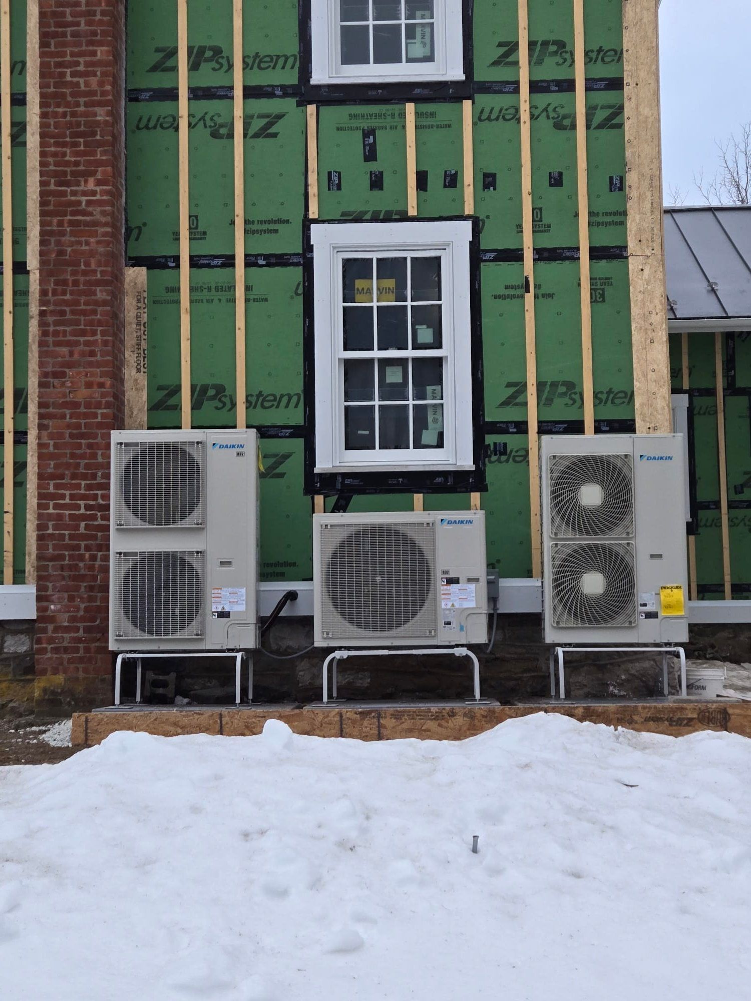 House exterior under construction with three outdoor HVAC units in front and snow on the ground