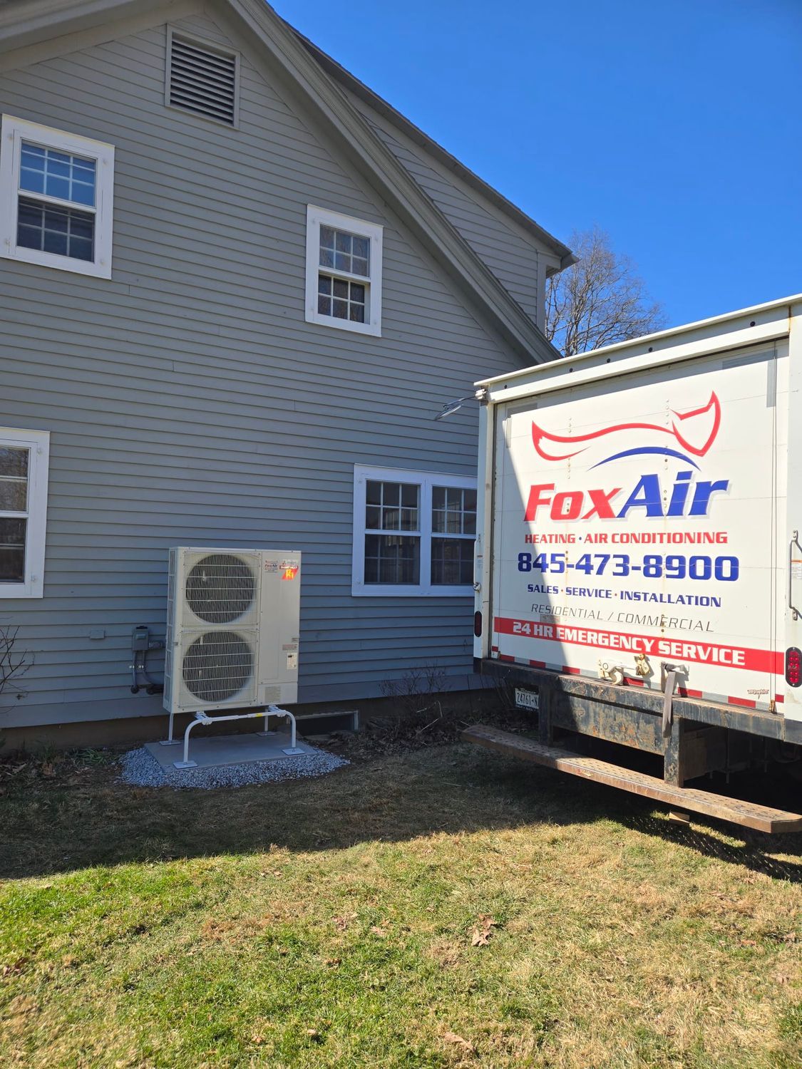 FoxAir HVAC service truck beside a gray house, with an outdoor AC unit in the yard.