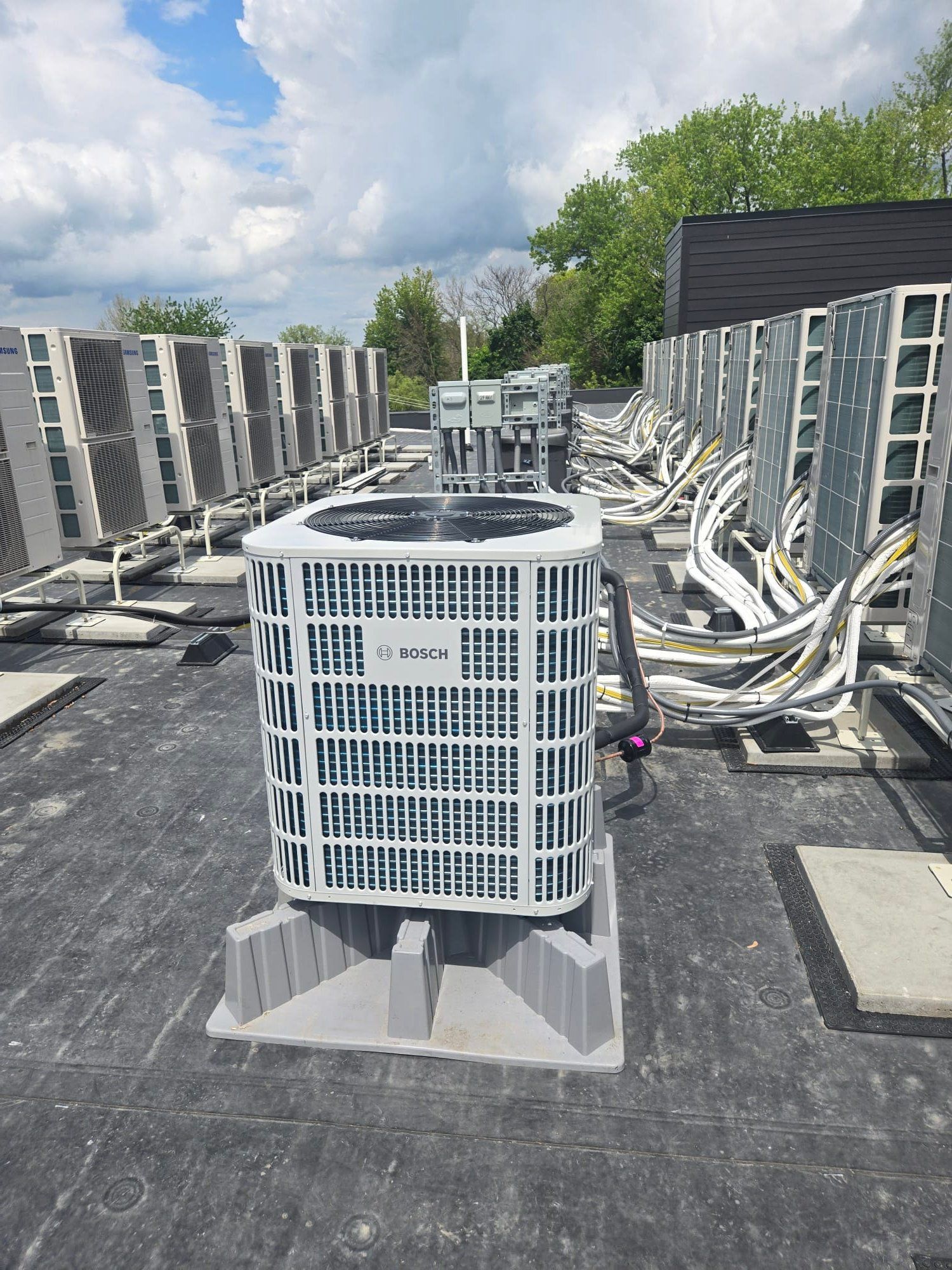 Rooftop row of outdoor air conditioning units under a partly cloudy sky