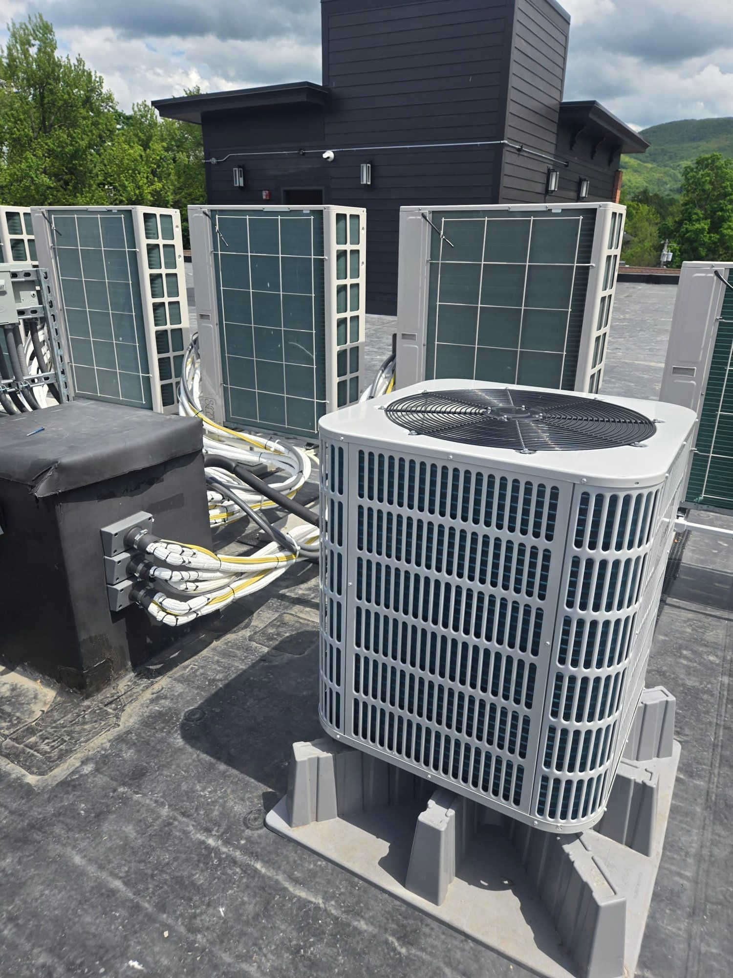 Rooftop HVAC units and ductwork beside a dark utility structure under a cloudy sky.