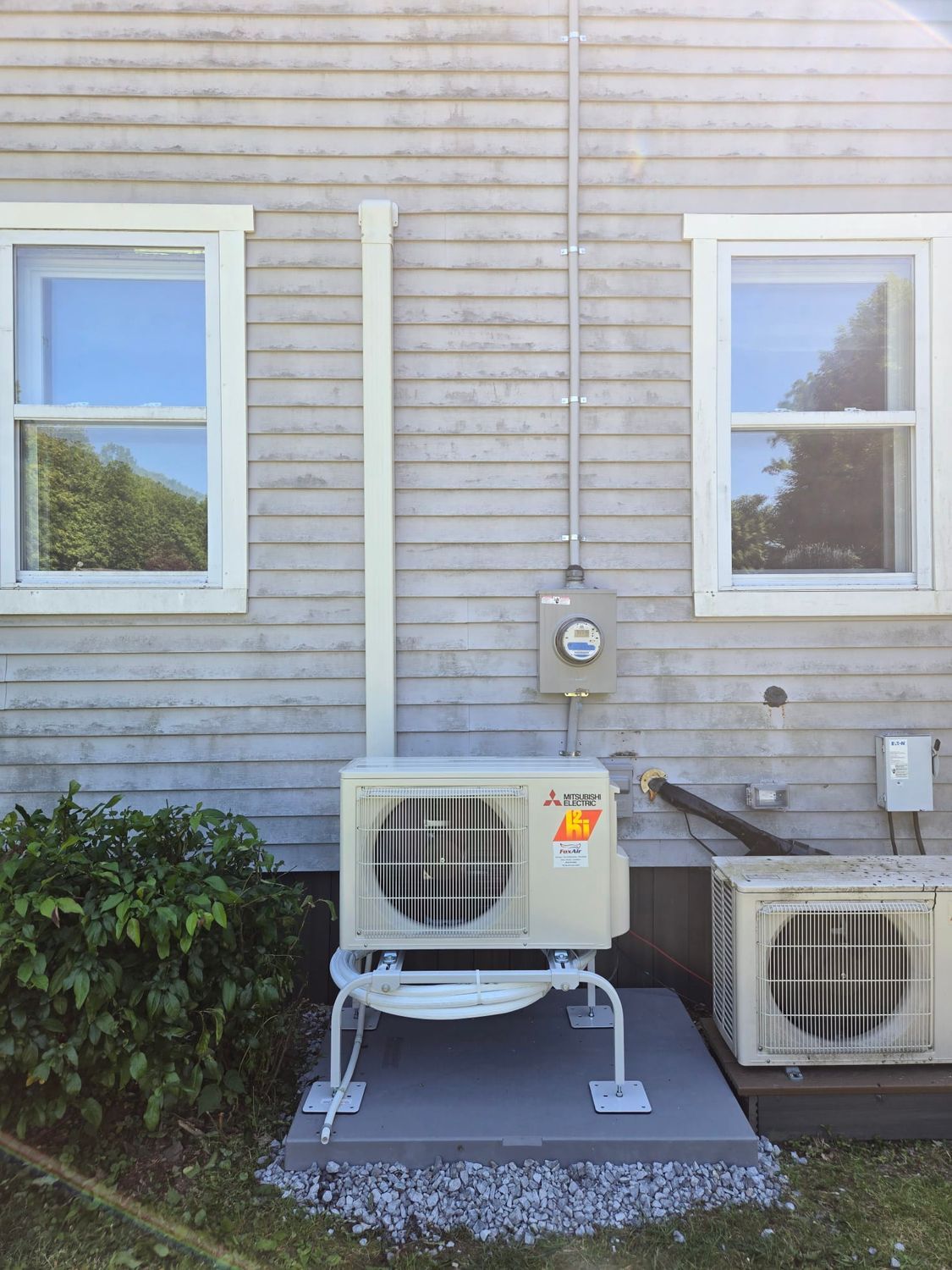 Outdoor HVAC unit on a concrete pad beside a house with an electric meter and another AC compressor.