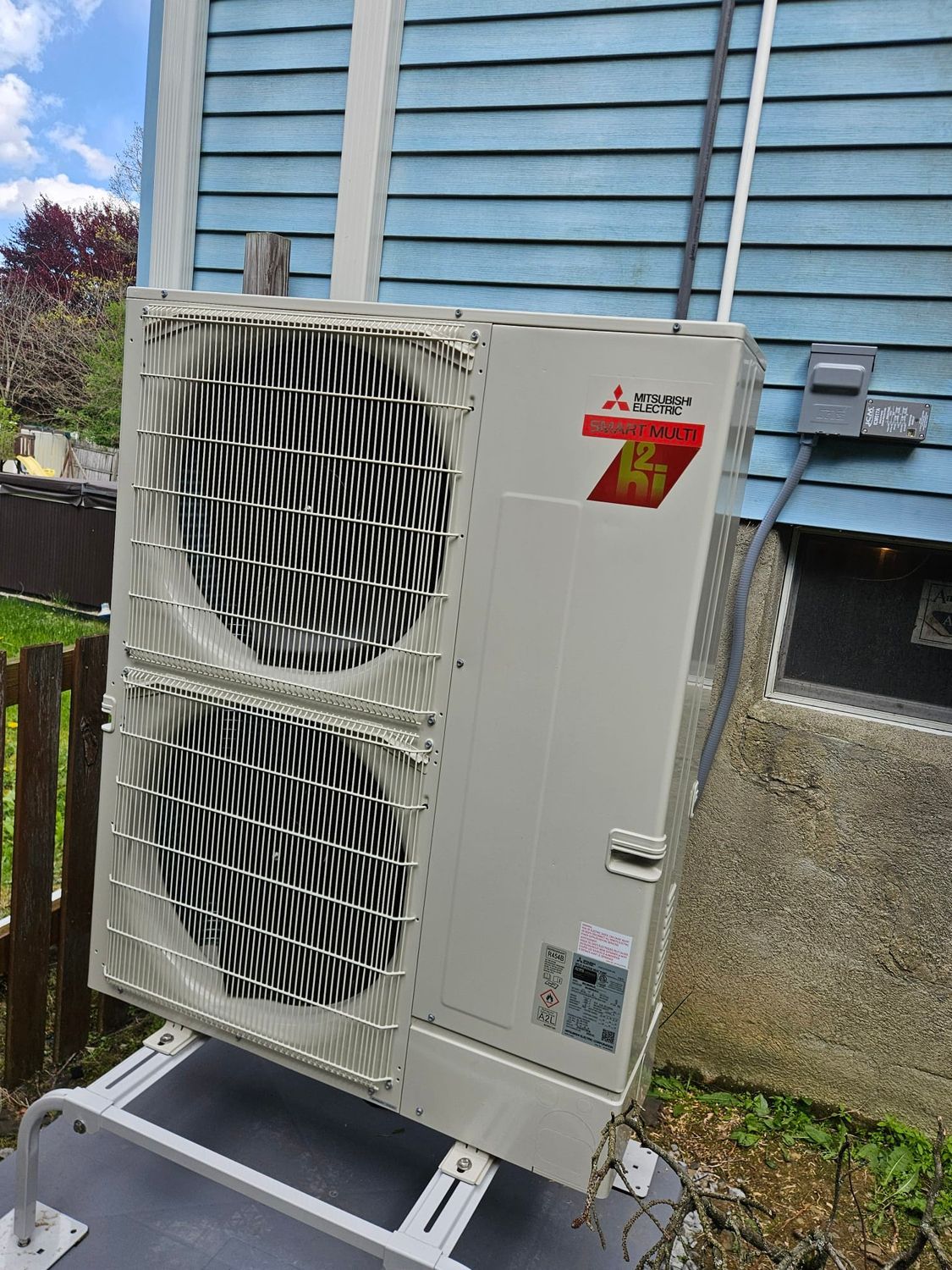 Outdoor HVAC unit with two large fans mounted beside a blue-sided building.