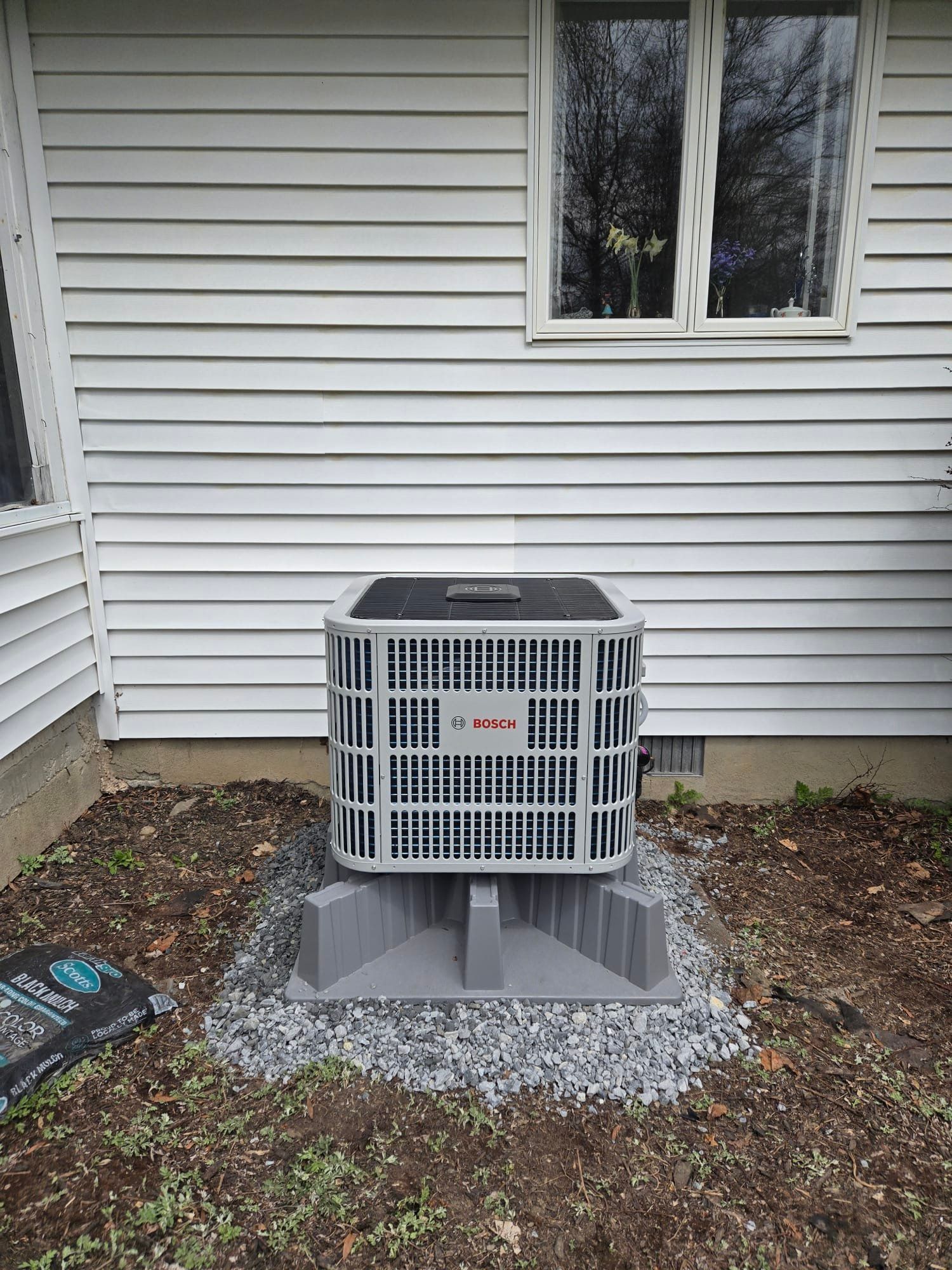 Outdoor air conditioner unit on a concrete pad beside a white house siding wall