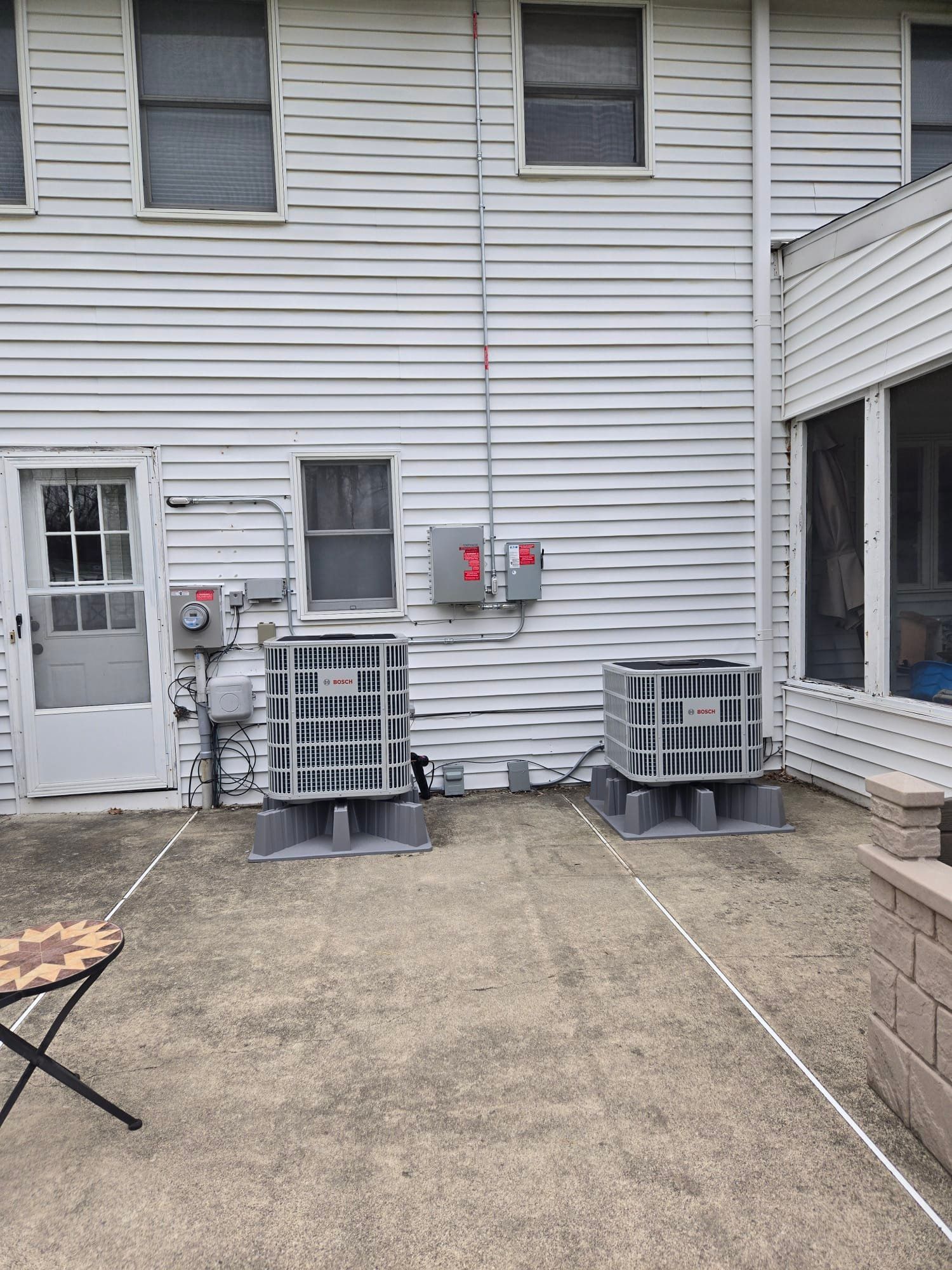 Backyard patio with two outdoor AC units against a white house wall and a small folding table.