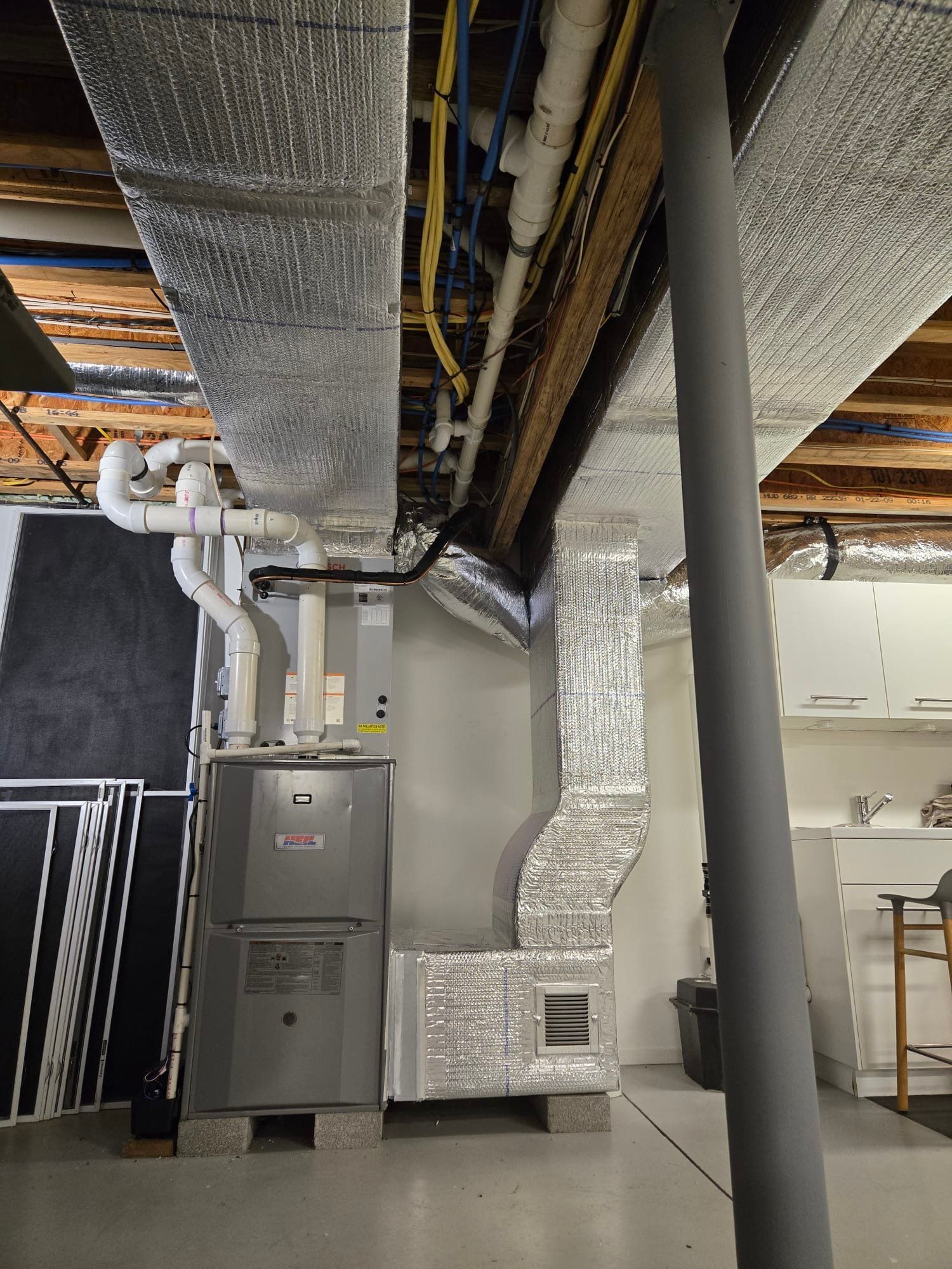 Basement utility room with exposed ducts, pipes, furnace, and water heater under a low ceiling