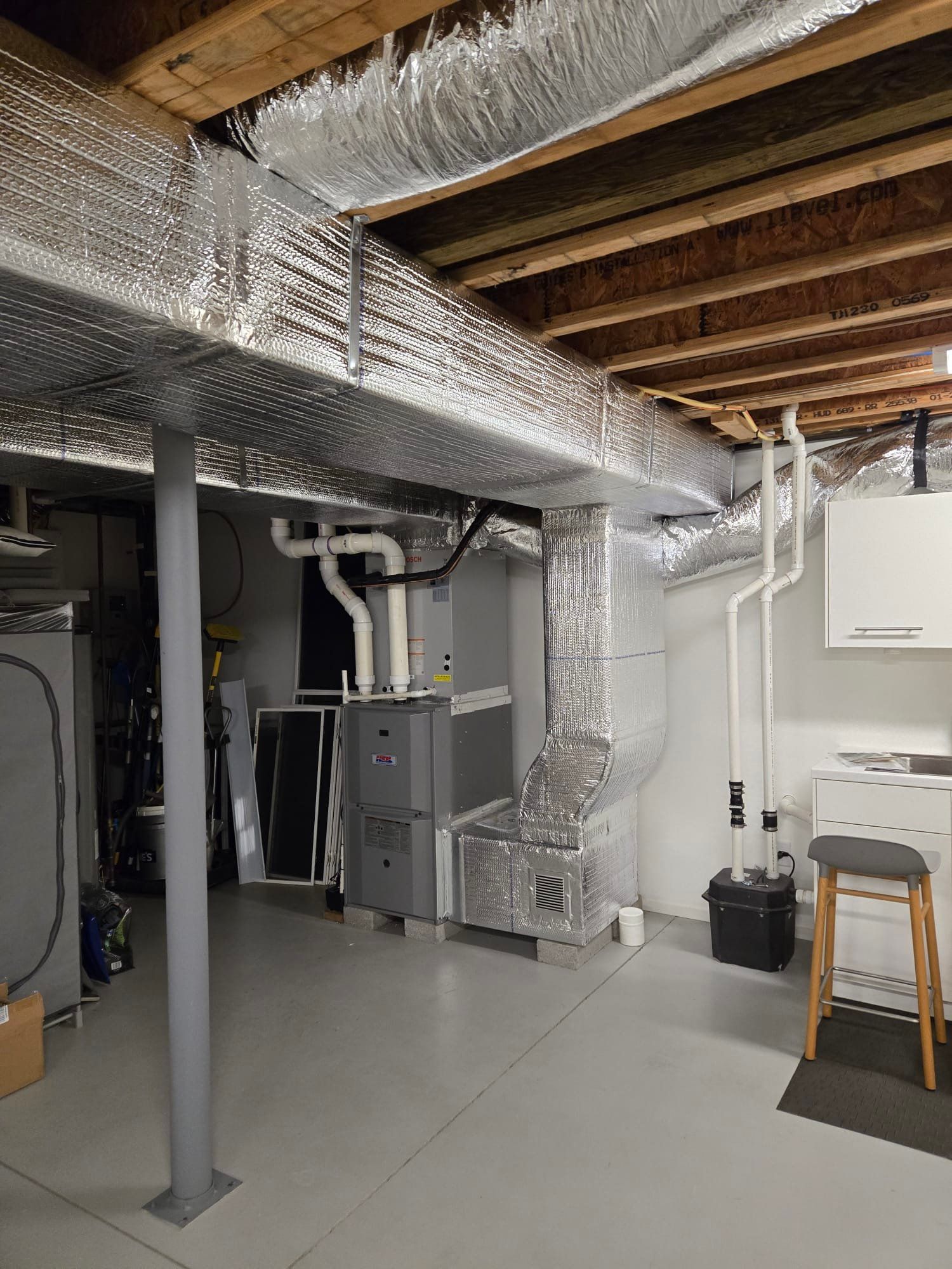 Basement utility room with HVAC ducts, furnace, exposed beams, and a laundry sink