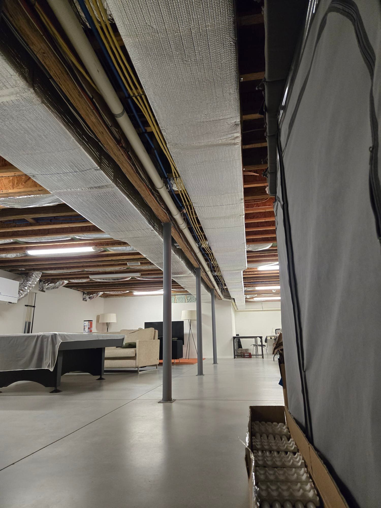 Interior of a minimalist room with concrete floor, exposed ceiling beams, and a lounge area in the back