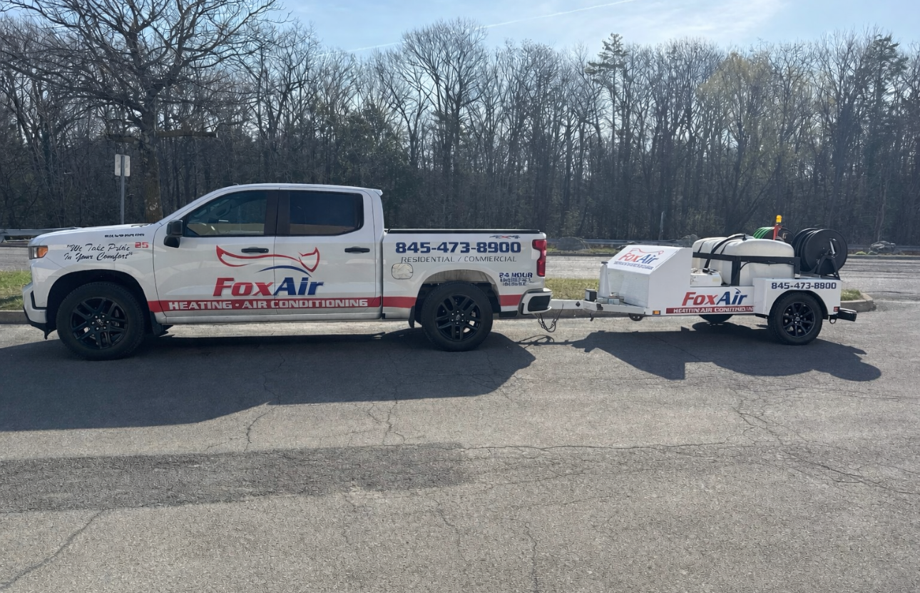 White Fox Air service pickup truck towing a white trailer in a parking lot with leafless trees behind.