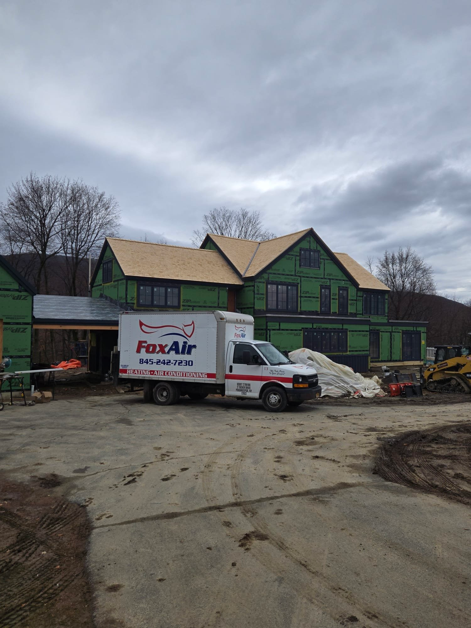 Green house under renovation with construction truck and materials in a muddy driveway under cloudy sky